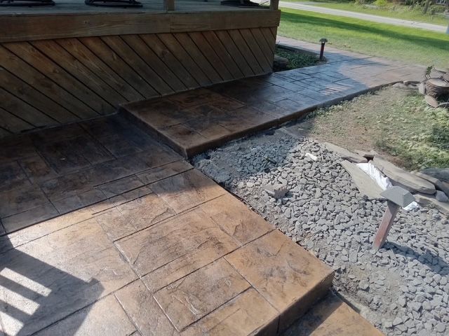 A two-story stucco house with a tiled roof, an attached garage, and a cobblestone driveway in a landscaped yard.