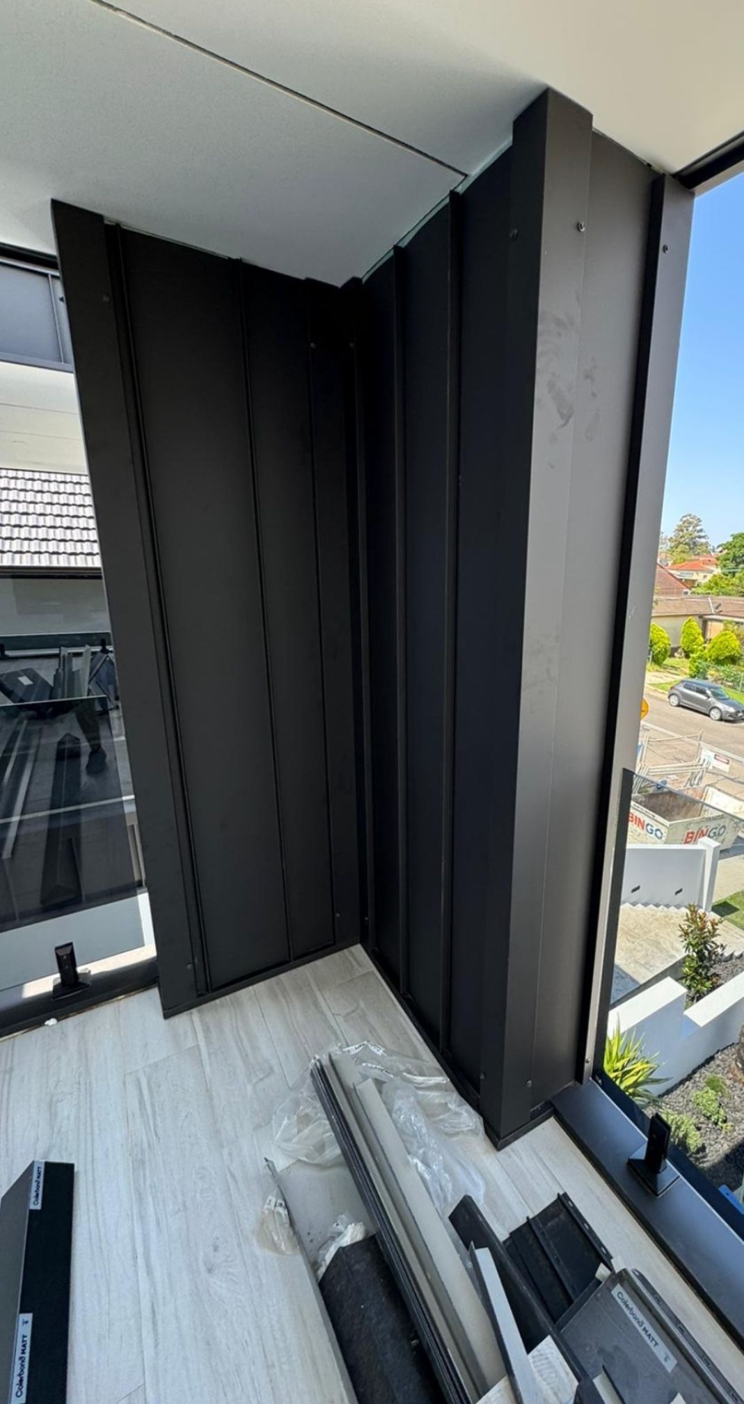 Black corner wall panels inside a modern building, beside a large window with city views. — McLuckie Metal Roofing In Lugarno, NSW