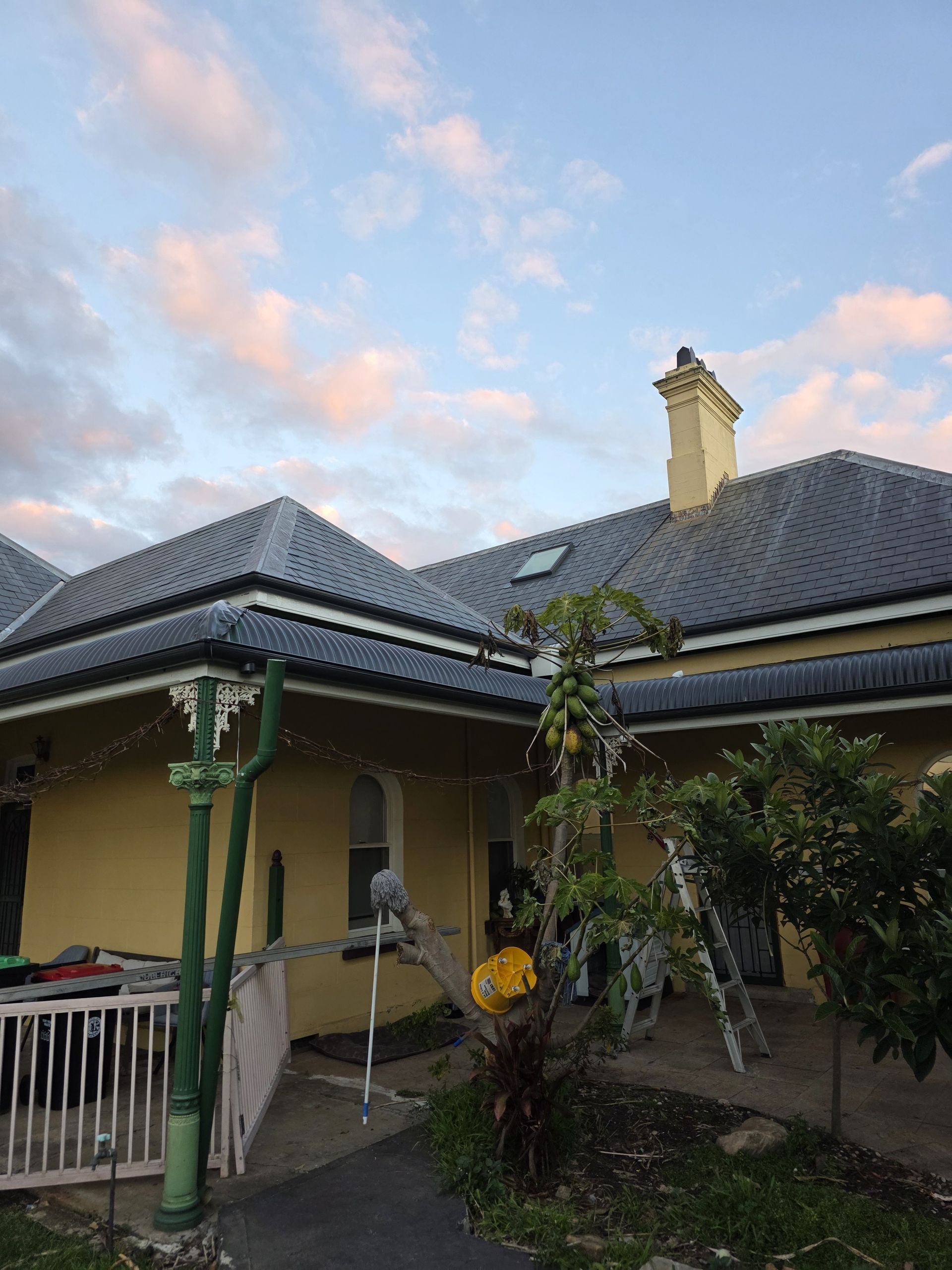 Yellow house with grey roof, front porch, and trees against a cloudy sky. — McLuckie Metal Roofing In Lugarno, NSW