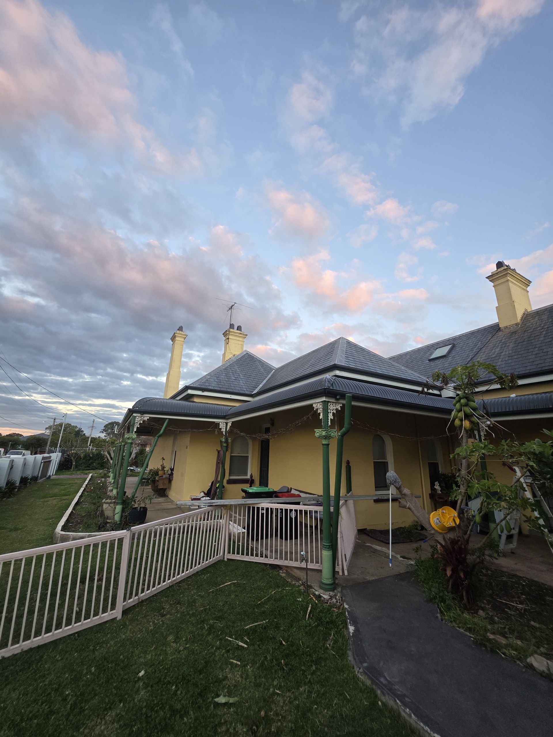 Yellow house with black roof and green accents under a cloudy, colourful sky. — McLuckie Metal Roofing In Lugarno, NSW