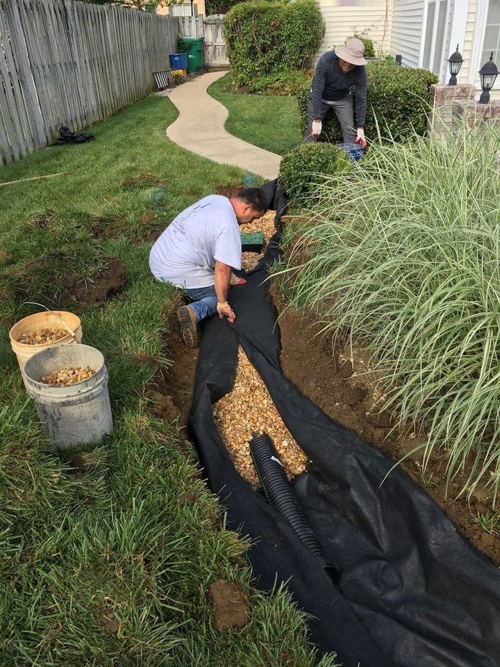 Two men are working on a drainage system in a backyard.
