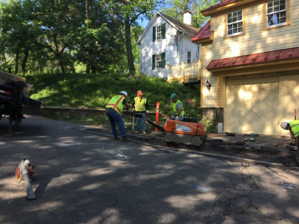 A group of construction workers are working on a driveway in front of a house.