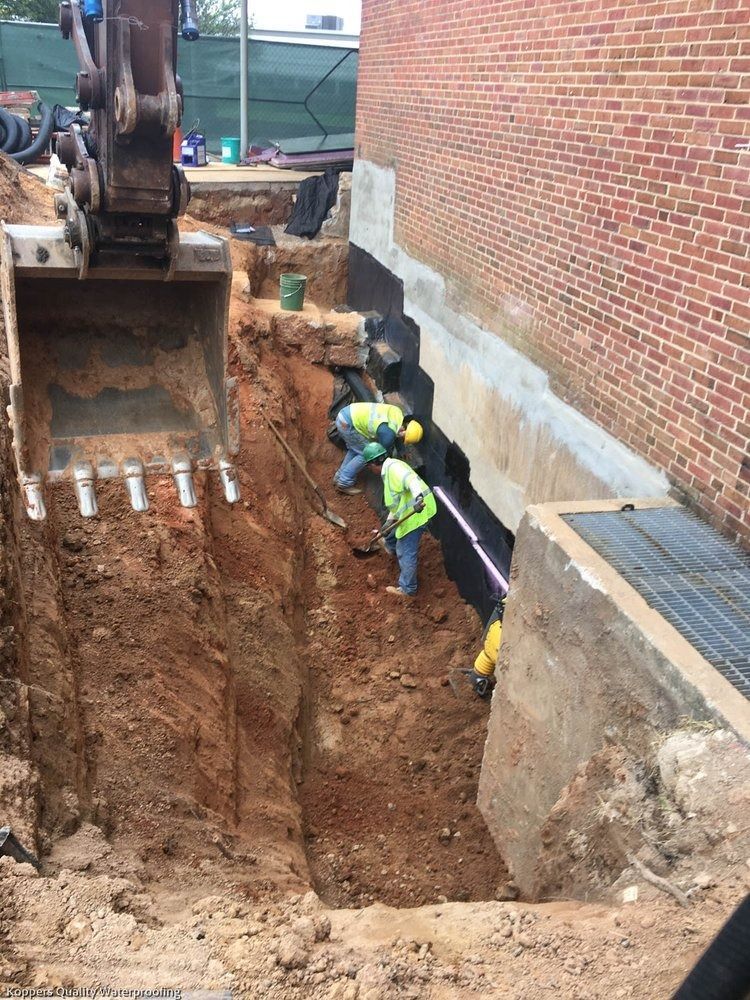 A group of construction workers are digging a trench in front of a brick building.
