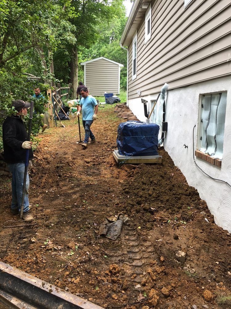 A group of people are digging in the dirt in front of a house.
