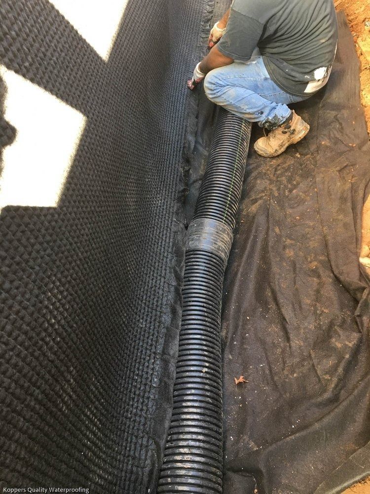 A man is kneeling down next to a black pipe.