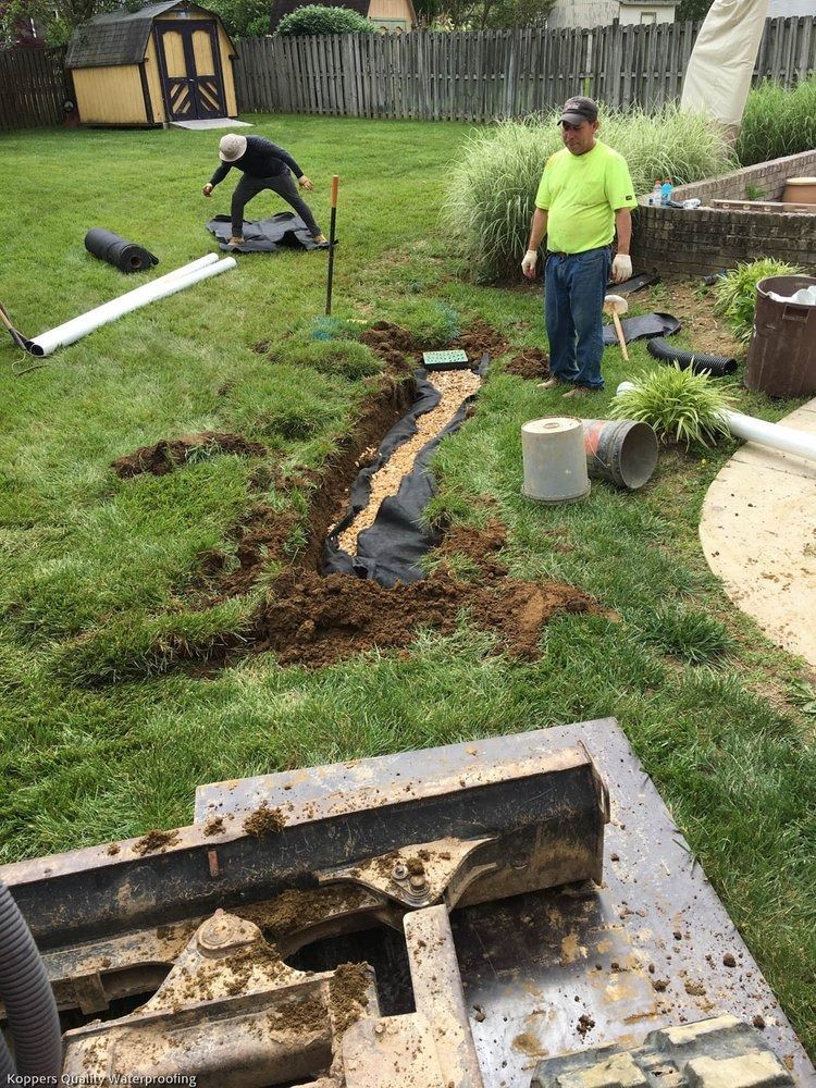 A man is working on a drainage system in a backyard.