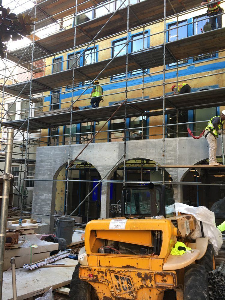 A yellow dump truck is parked in front of a building under construction.