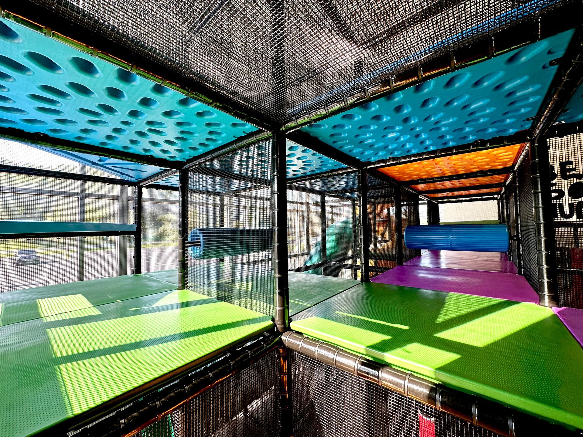 A colorful indoor playground with green , blue , and purple tables and a slide.