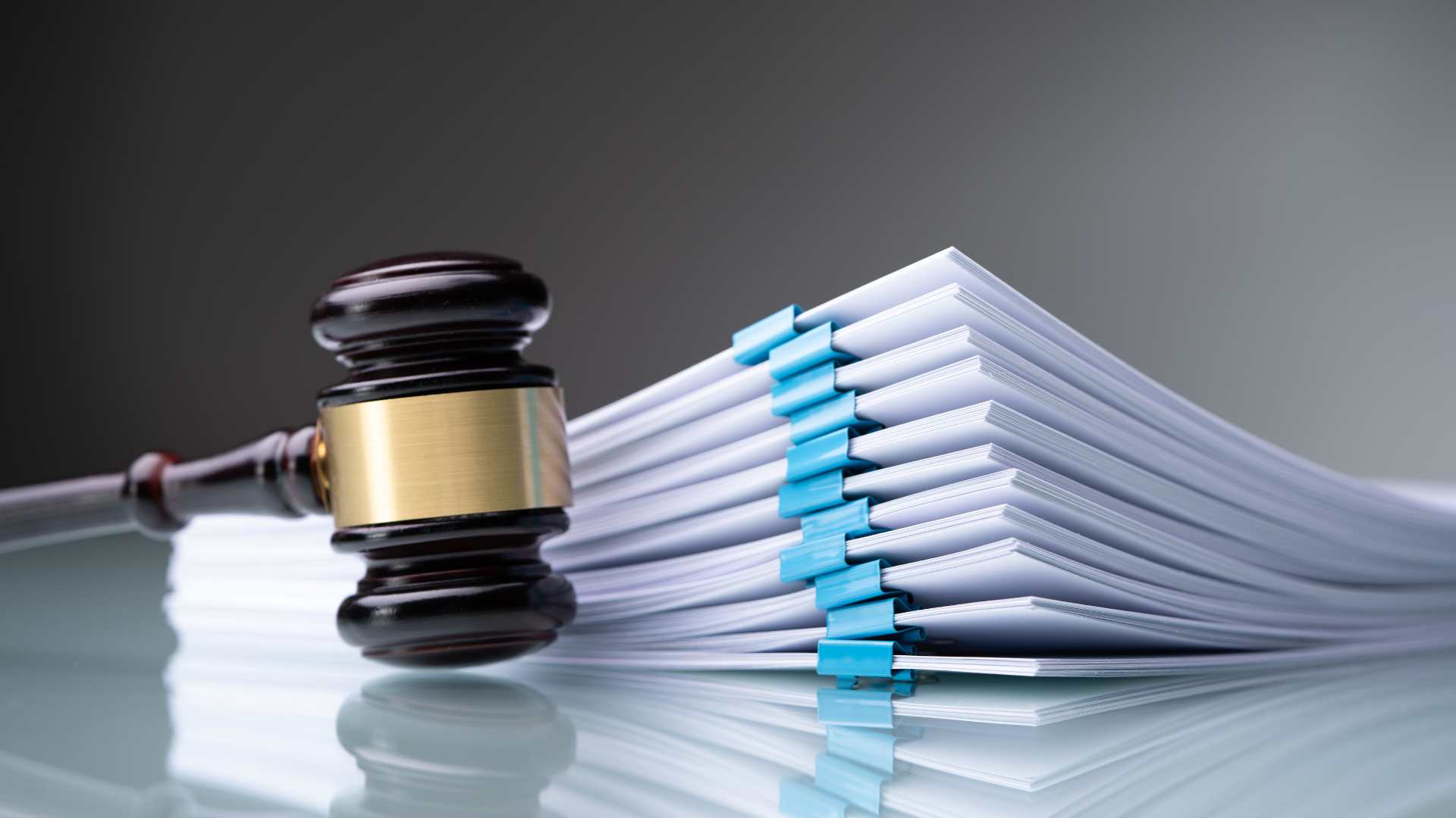 Wooden gavel next to a stack of white documents held together with blue binder clips.
