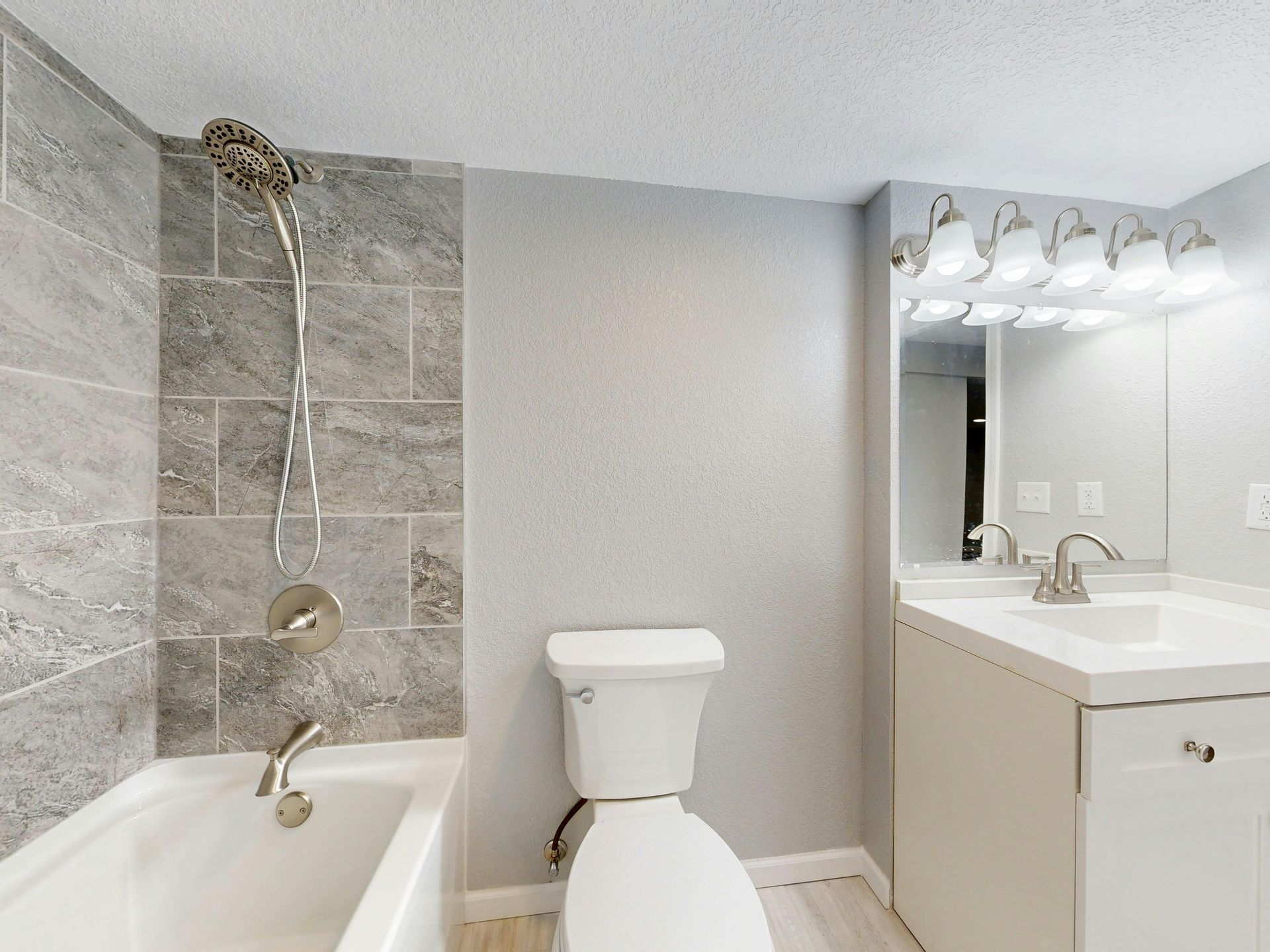 Bathroom with gray tile shower, white toilet, vanity, and neutral-colored walls.