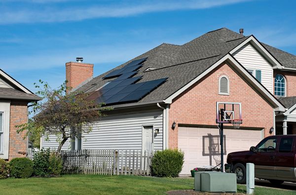 A red truck is parked in front of a brick house with solar panels on the roof.