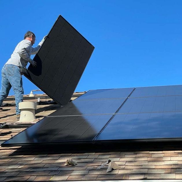 A man is installing solar panels on the roof of a house.