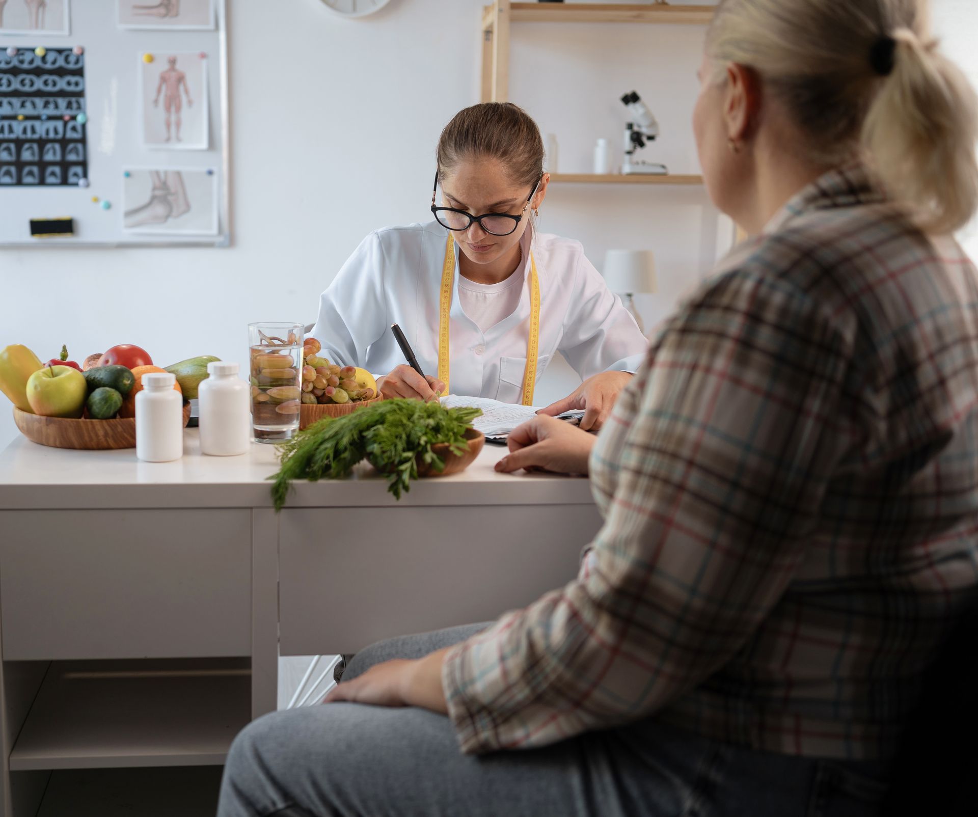 Dietitian in white coat reviewing notes with a client at a desk with fruits, vegetables and supplements.