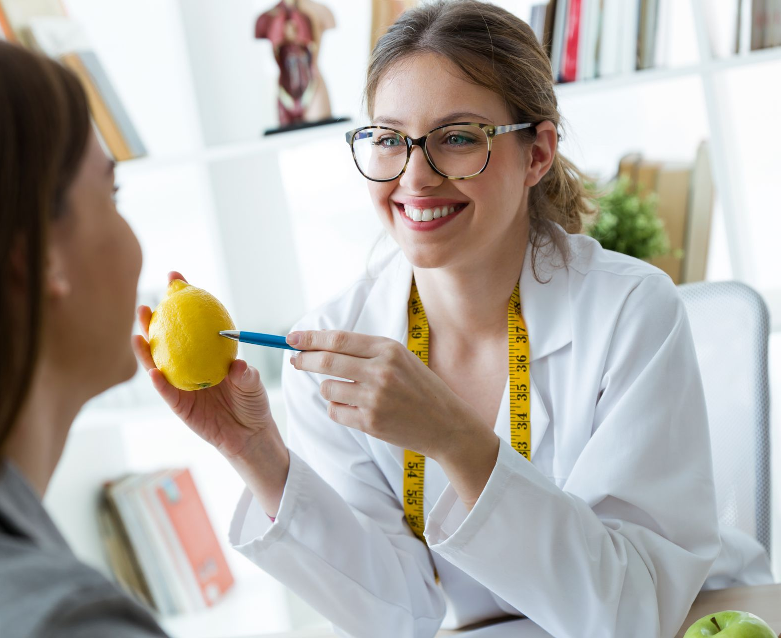 Dietitian pointing to a lemon, speaking with a client in an office.