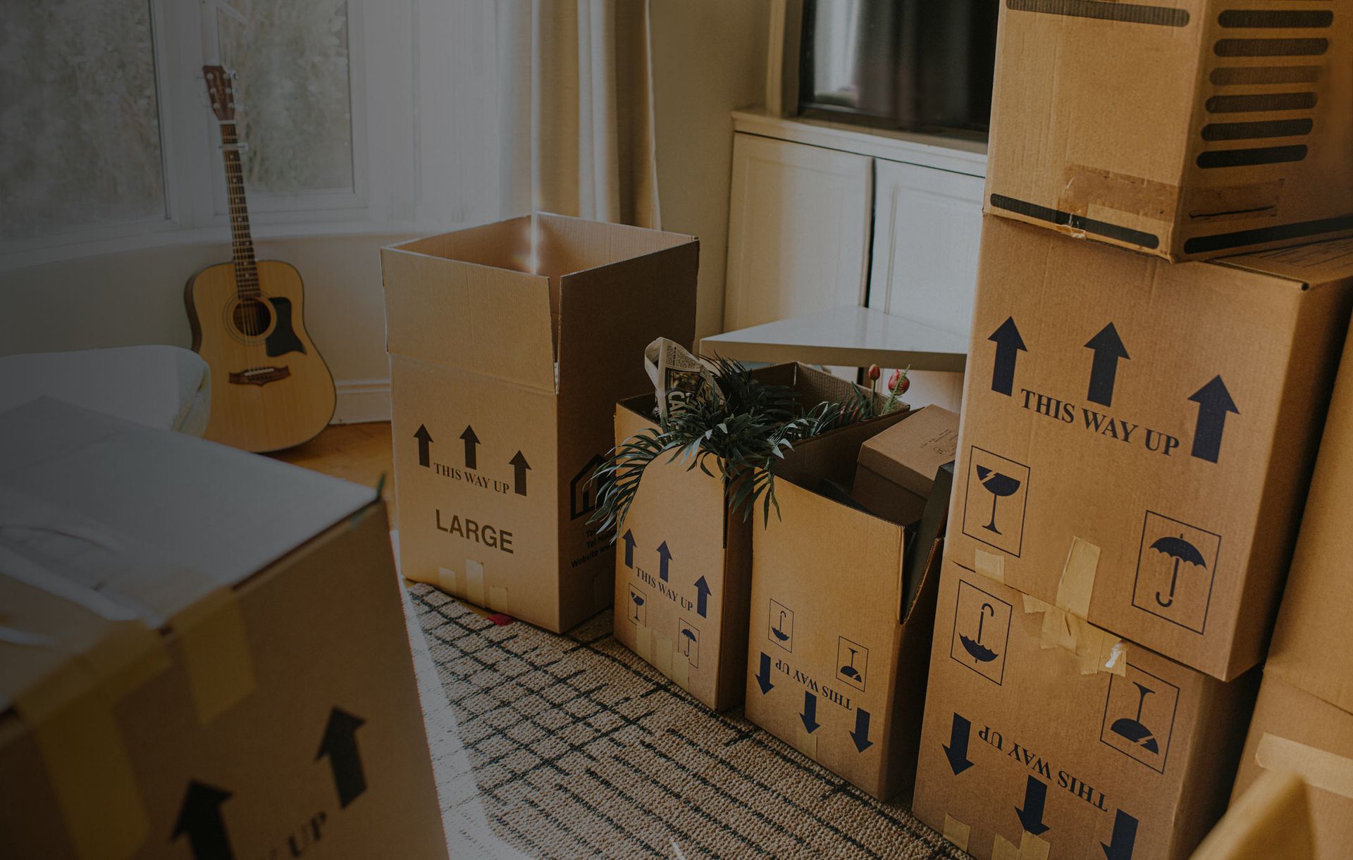 A room filled with cardboard boxes and a guitar.