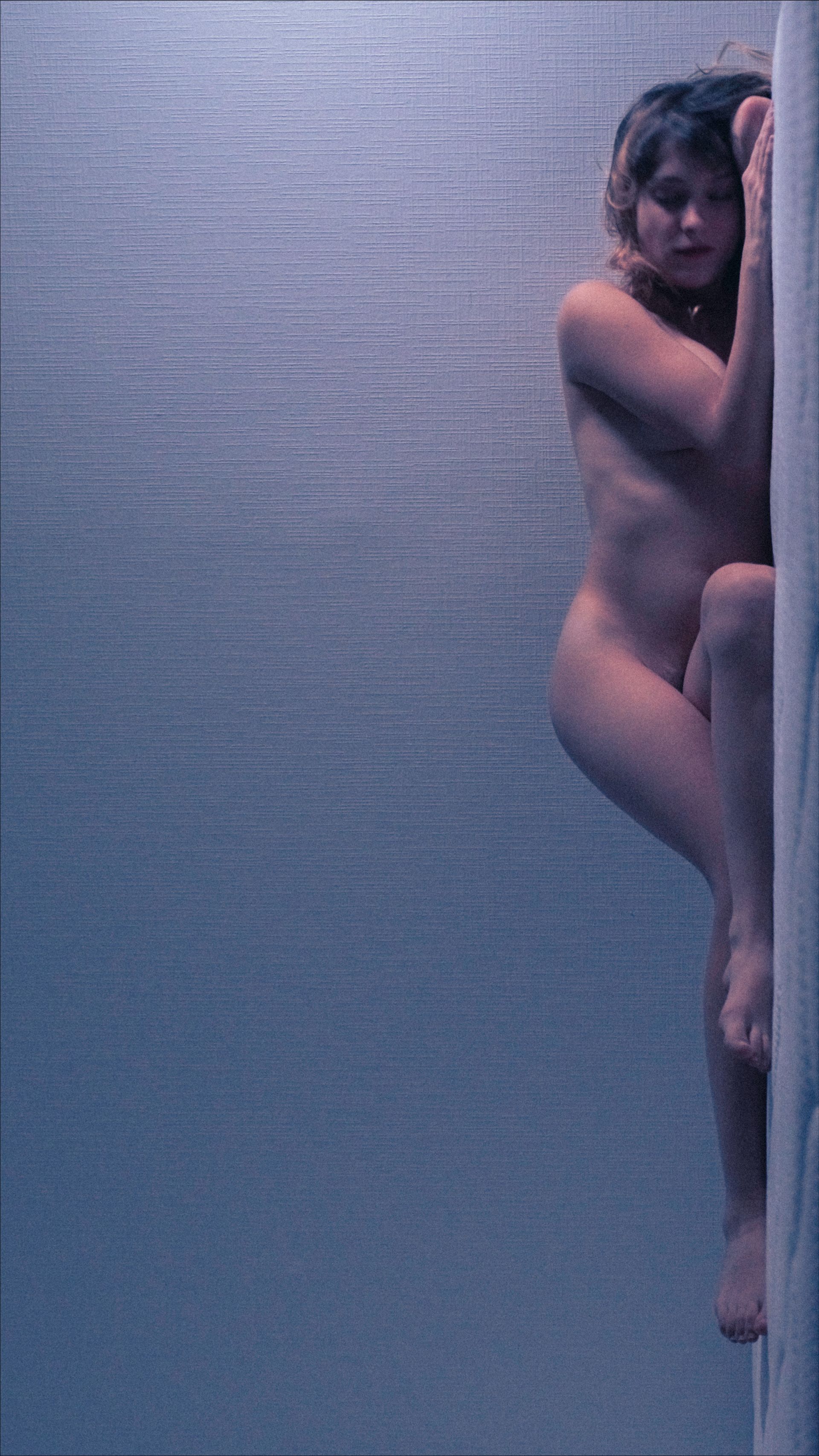 Naked person leaning against a wall, in a blue-toned environment.