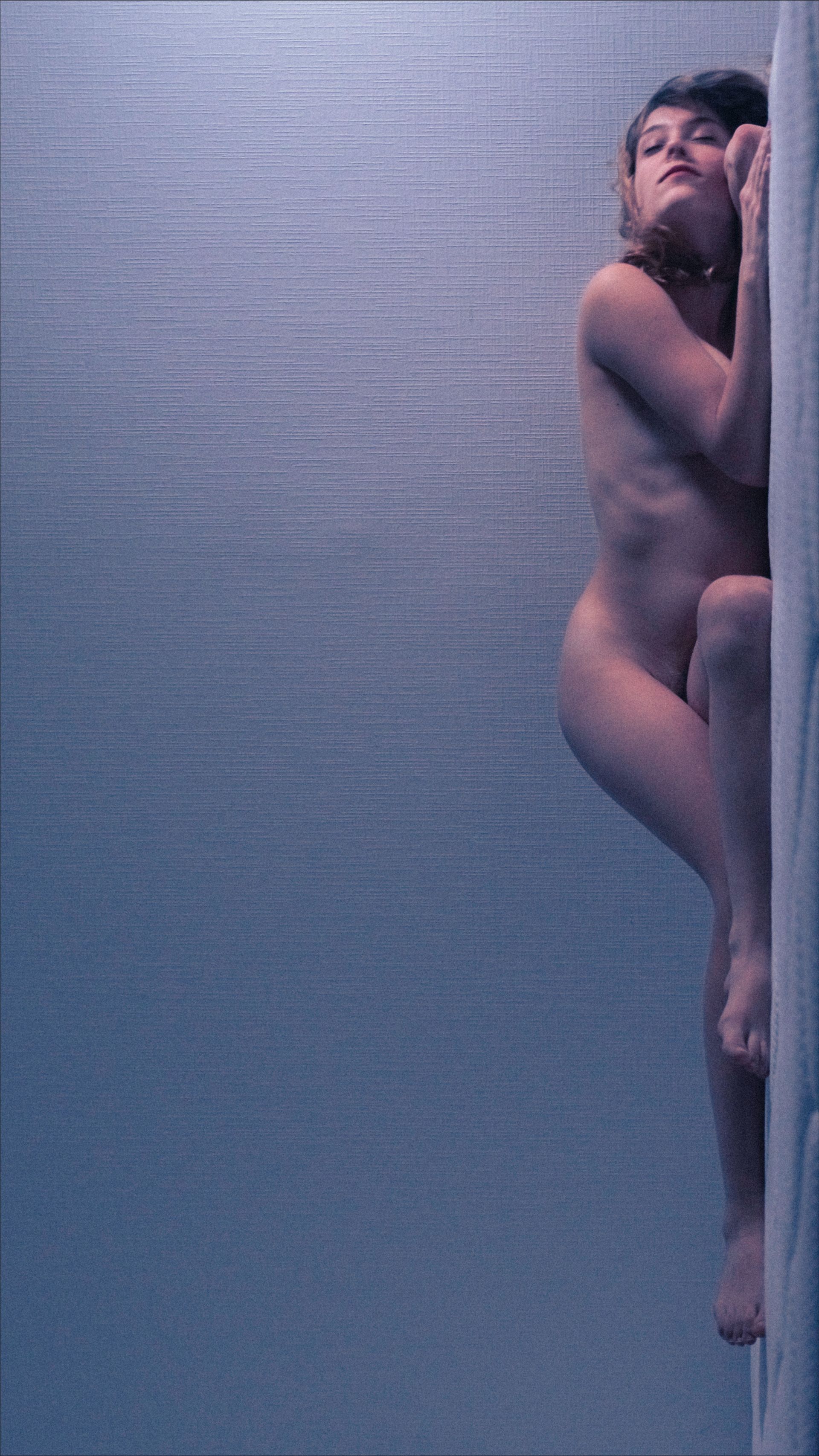Nude person underwater, clinging to a white wall. The water is a dark blue.