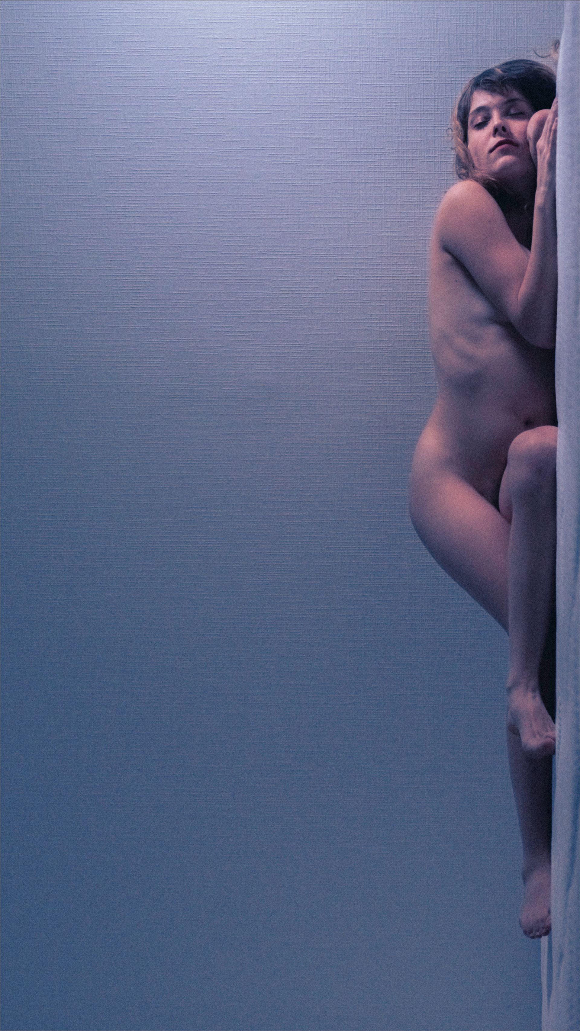 Naked person clinging to wall, eyes closed, body partially visible, pale blue background.