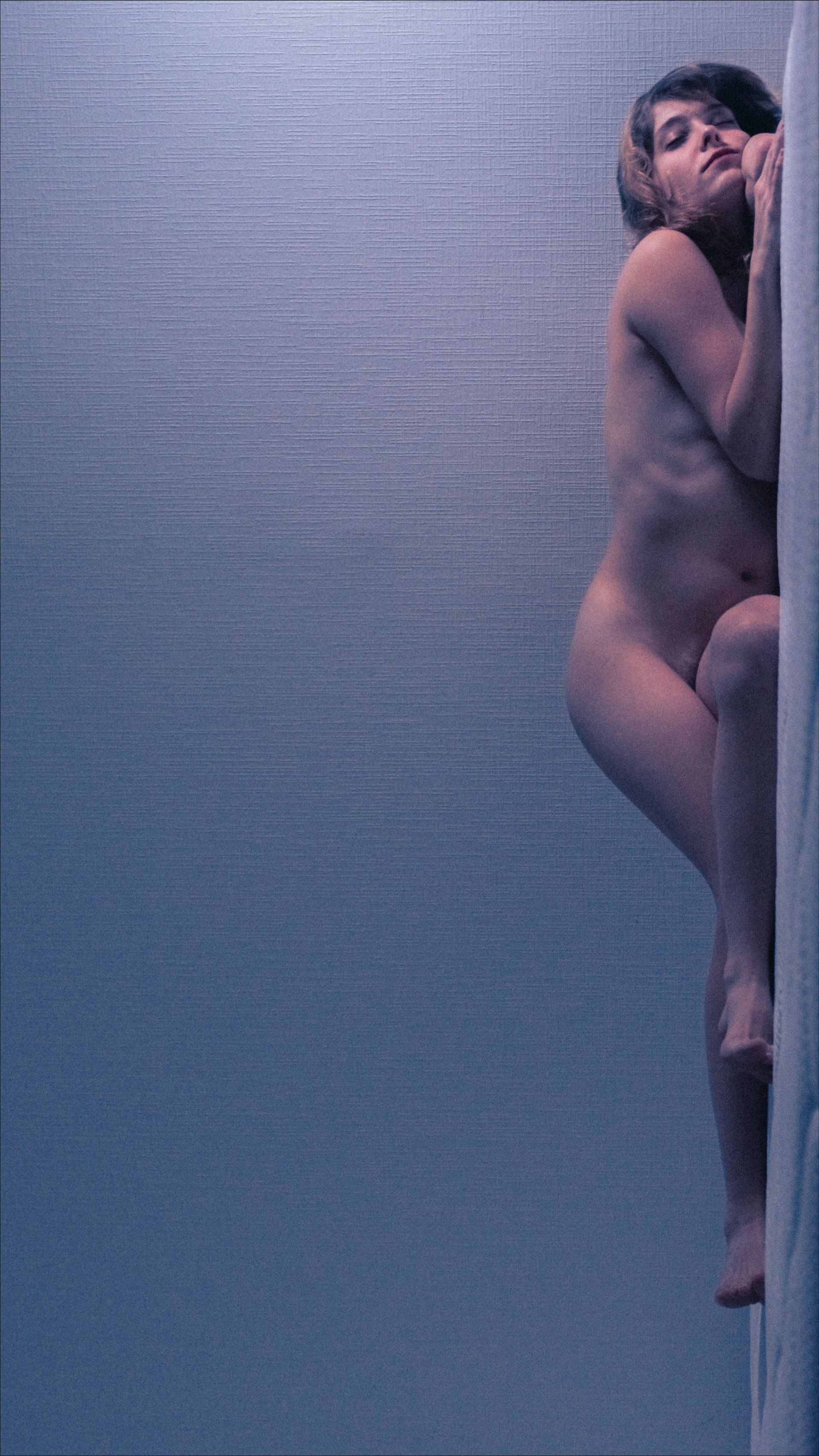Naked person climbs a textured, light-colored surface with a blue background.