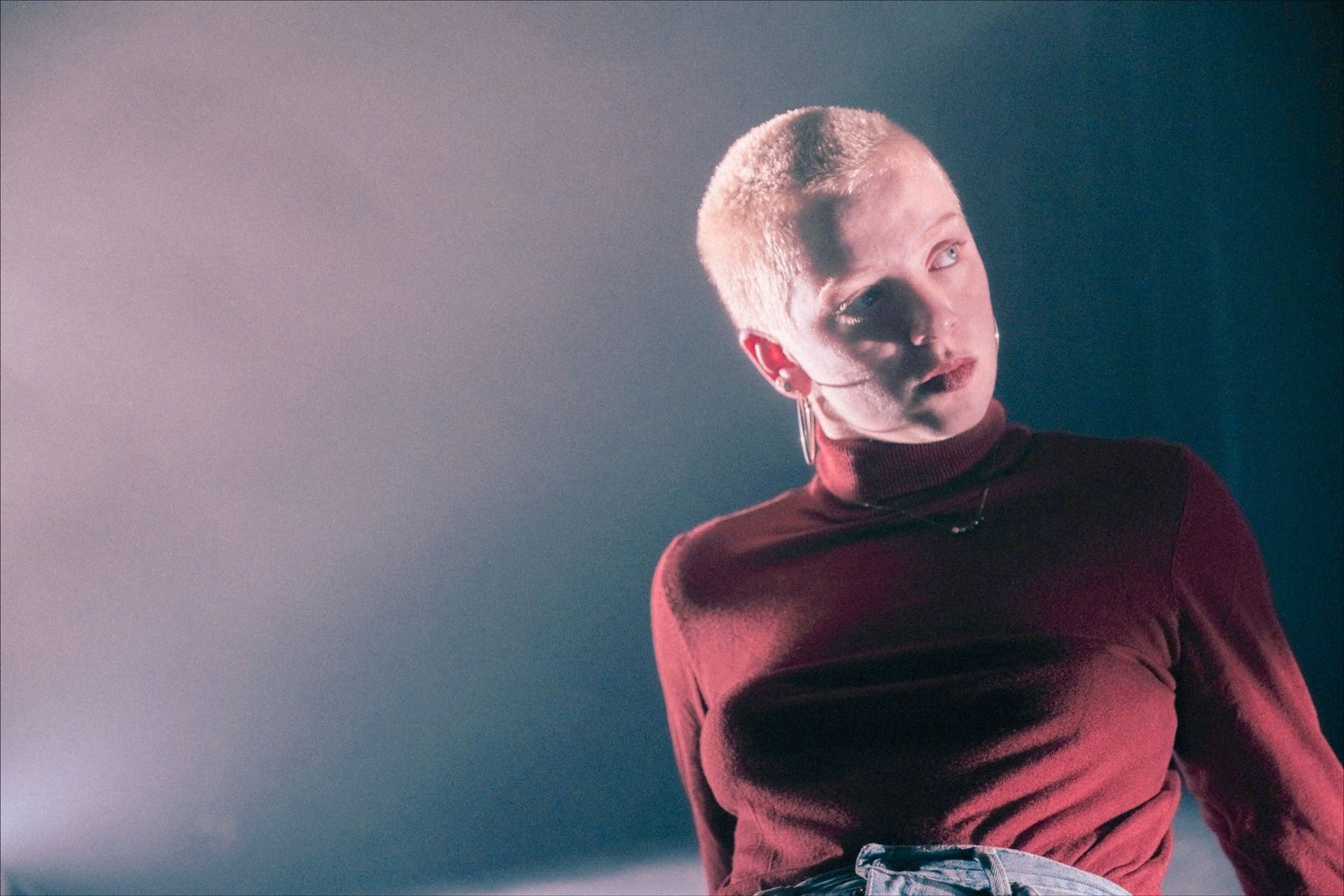 Person with shaved head wearing red turtleneck, looking upward with a serious expression.