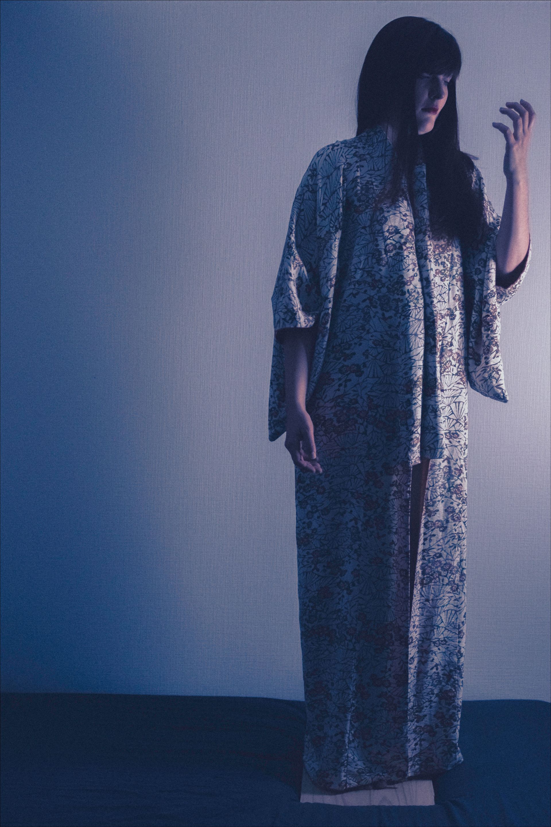 Woman in patterned clothing, hands clawed, against a blue-toned background.