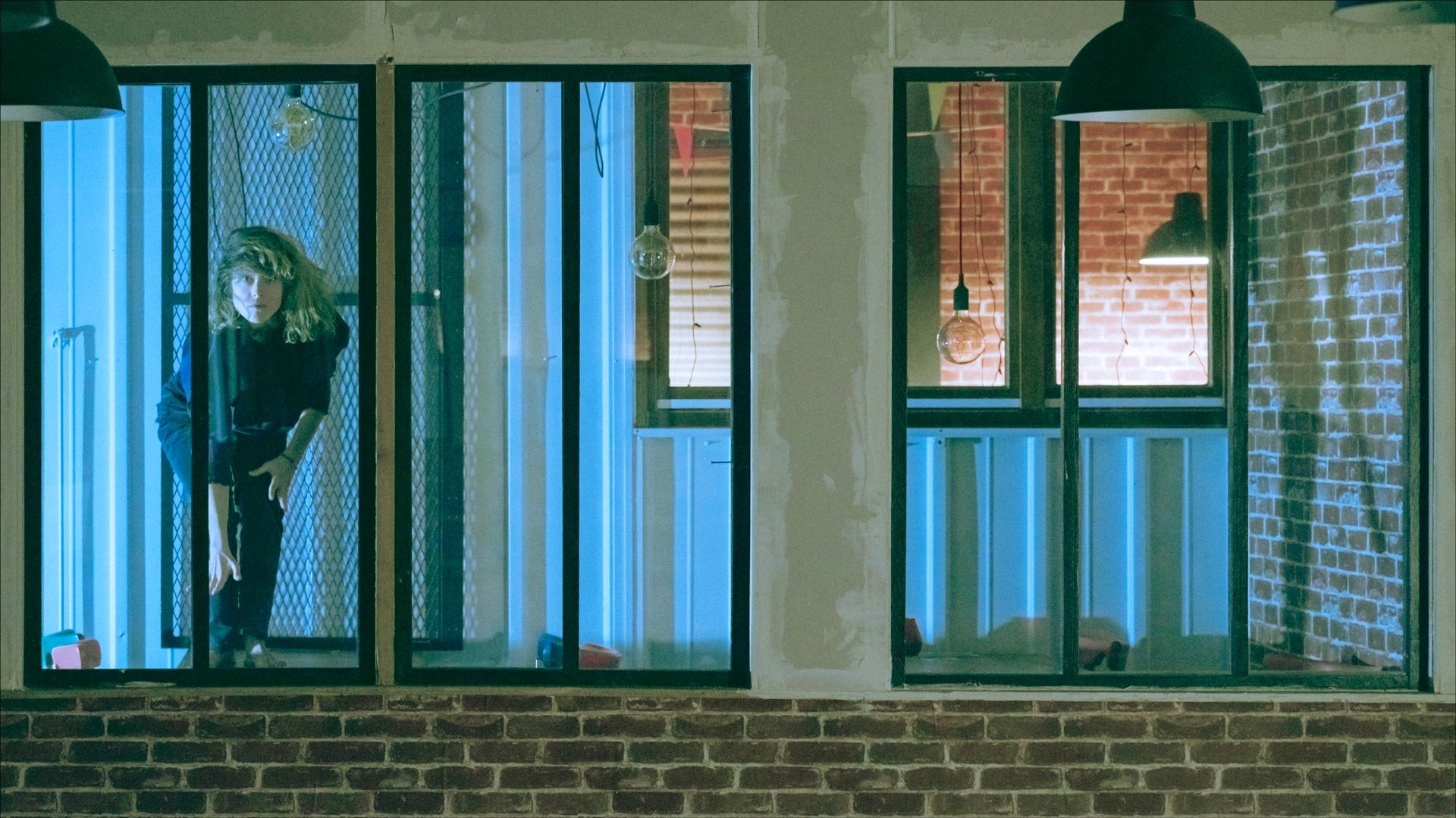 Person standing in a blue-lit room, visible through a window, brick wall below.