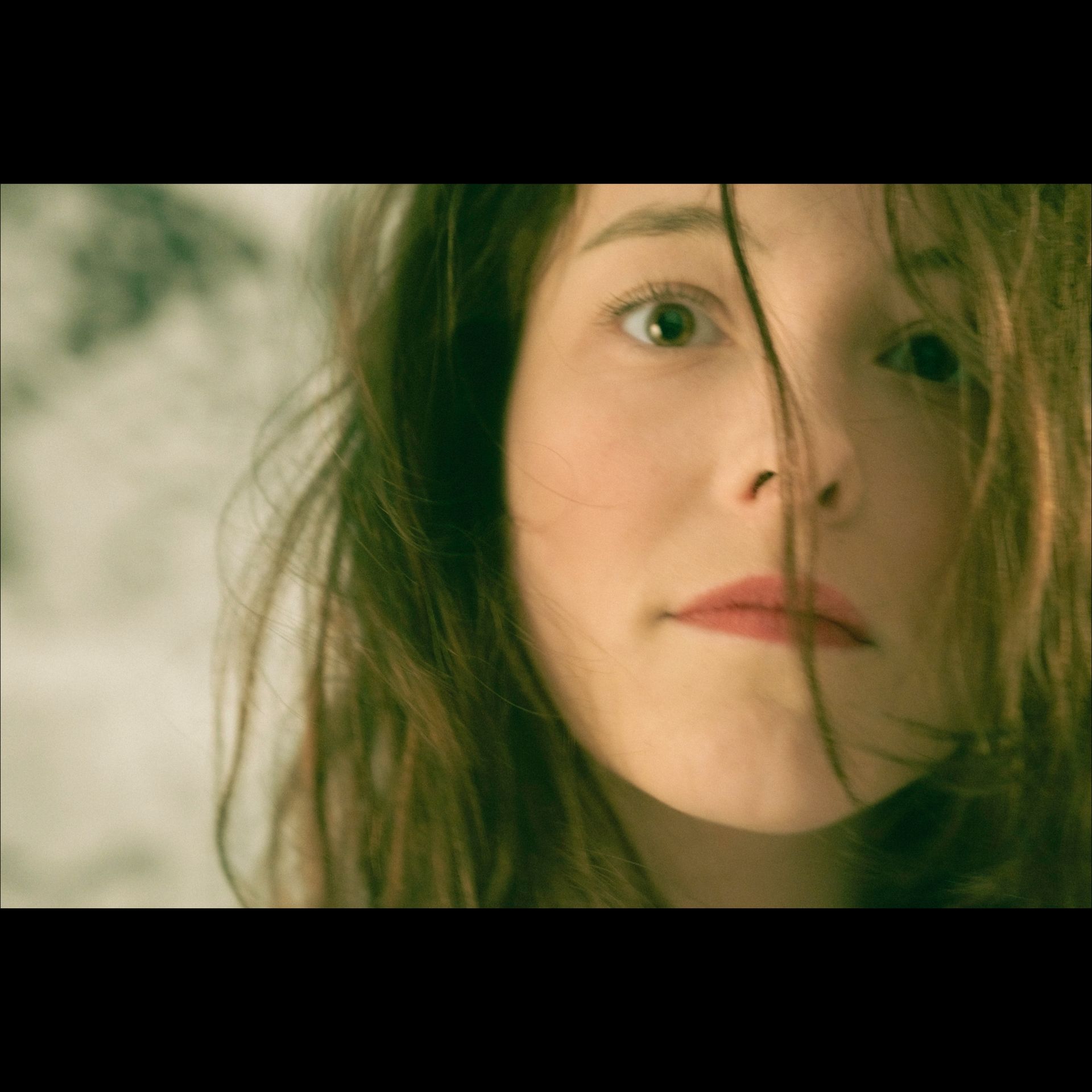 Woman with brown hair, looking at the viewer. Some hair falls over her face. Soft lighting.