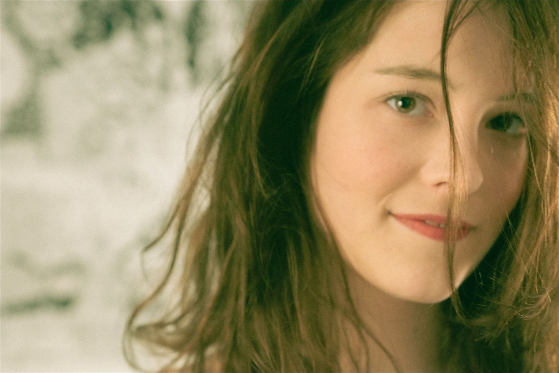 Woman with wavy brown hair, smiling, partially obscuring her face.