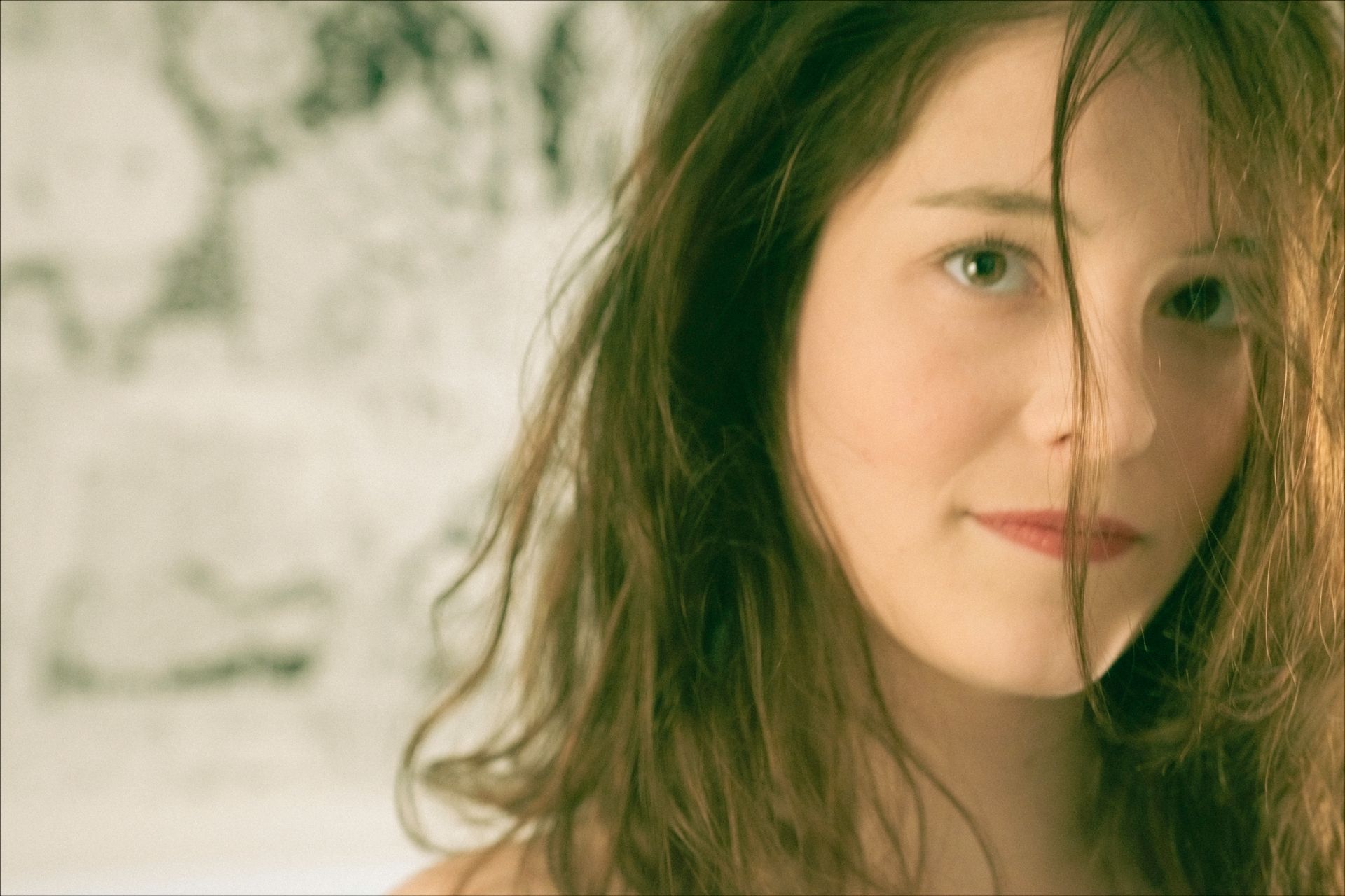 Woman with wavy brown hair, looking slightly to the side with a soft smile; background is out of focus.