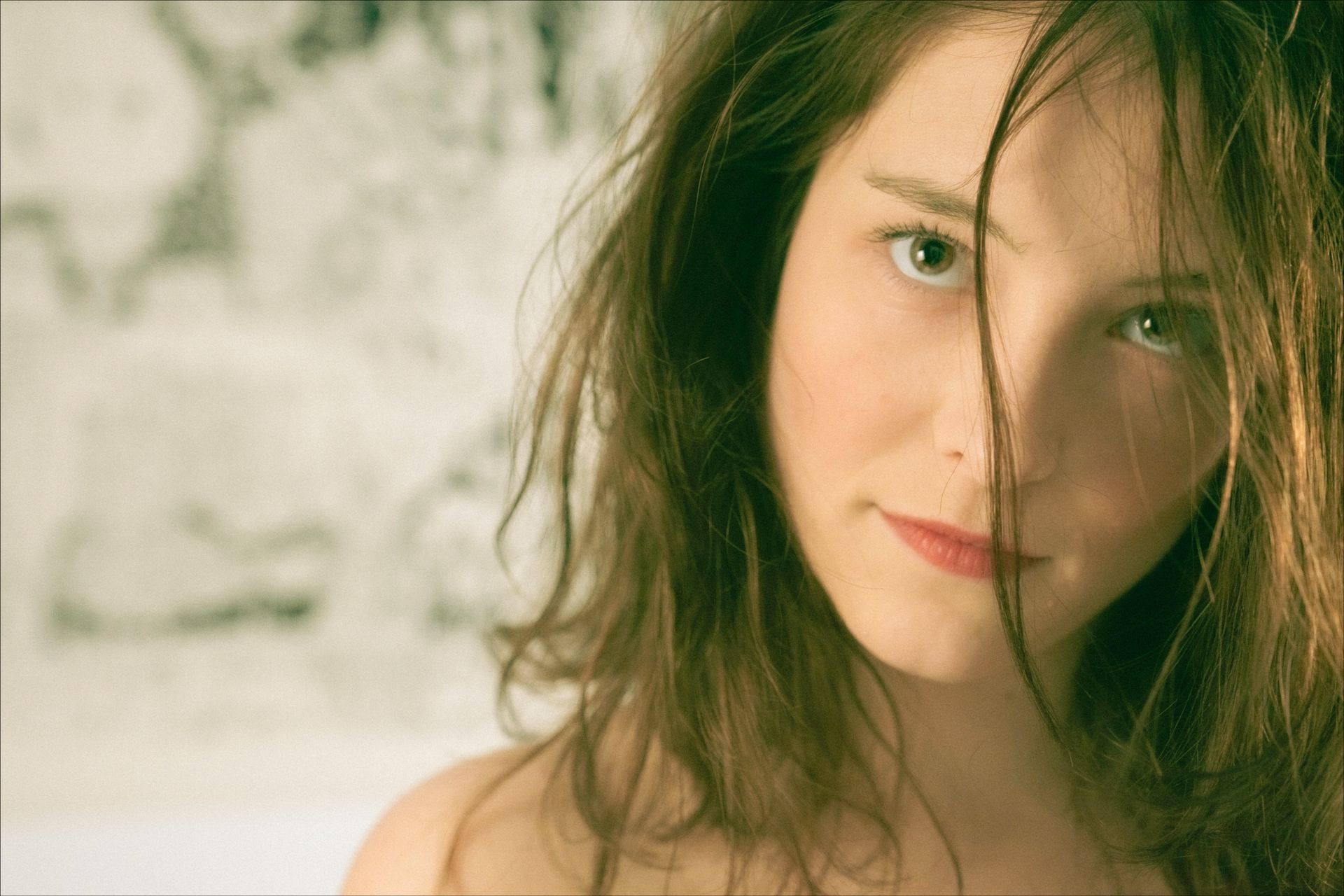Woman with tousled brown hair, looking intently at the viewer. Soft lighting, blurred background.