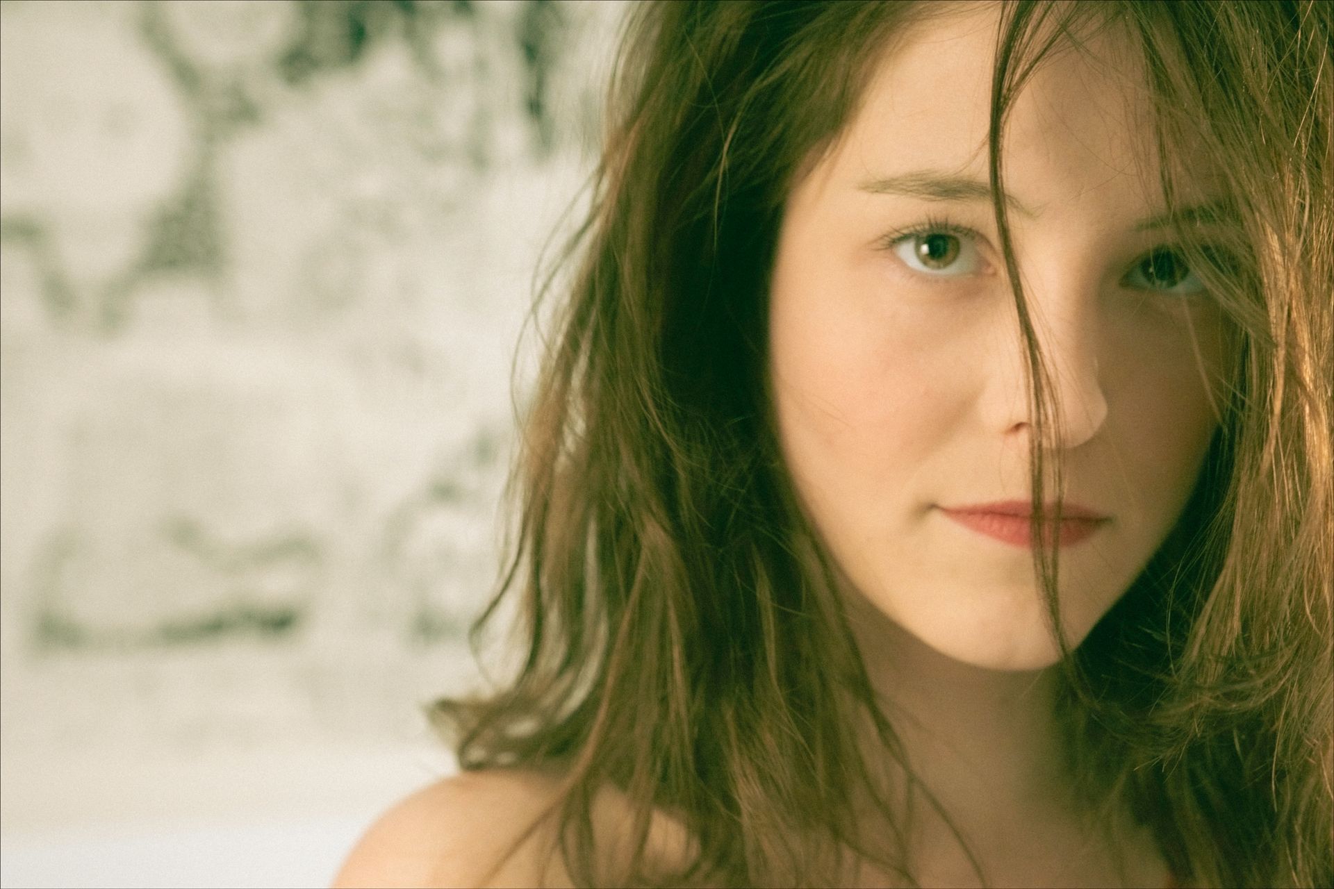 Woman with long brown hair, looking at the camera. Light skin, red lips, soft focus.