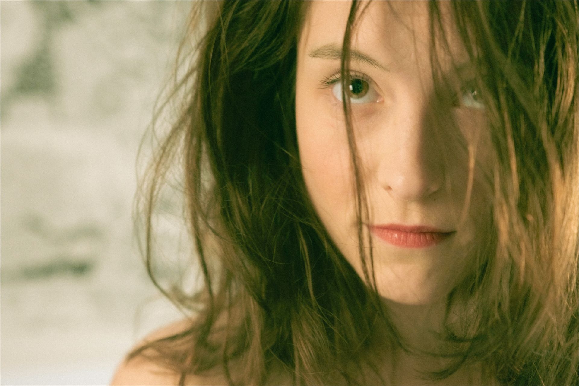 Woman with messy brown hair, looking directly at the viewer. Soft lighting, blurred background.