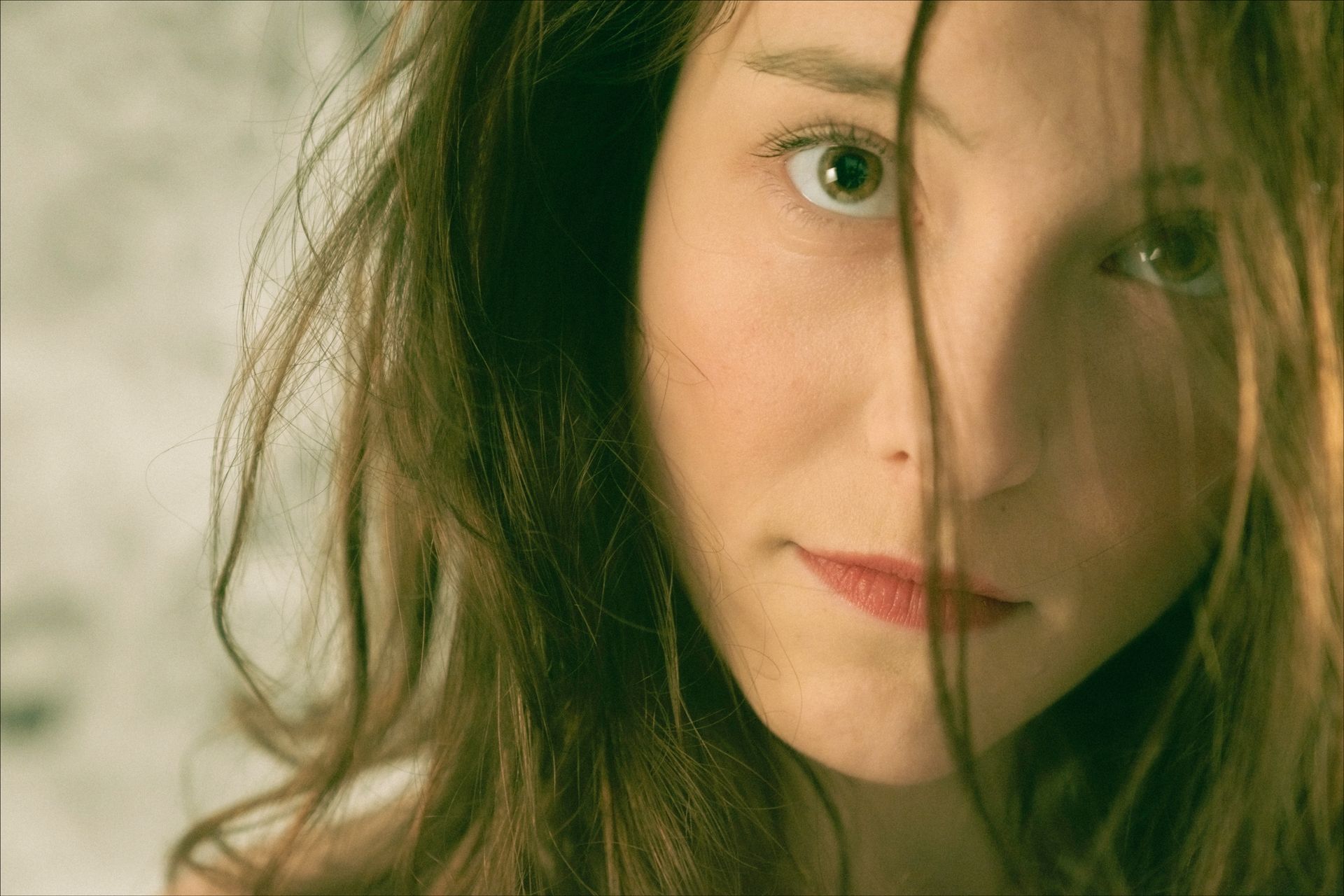 Woman with hair partially covering her face, looking at the viewer.