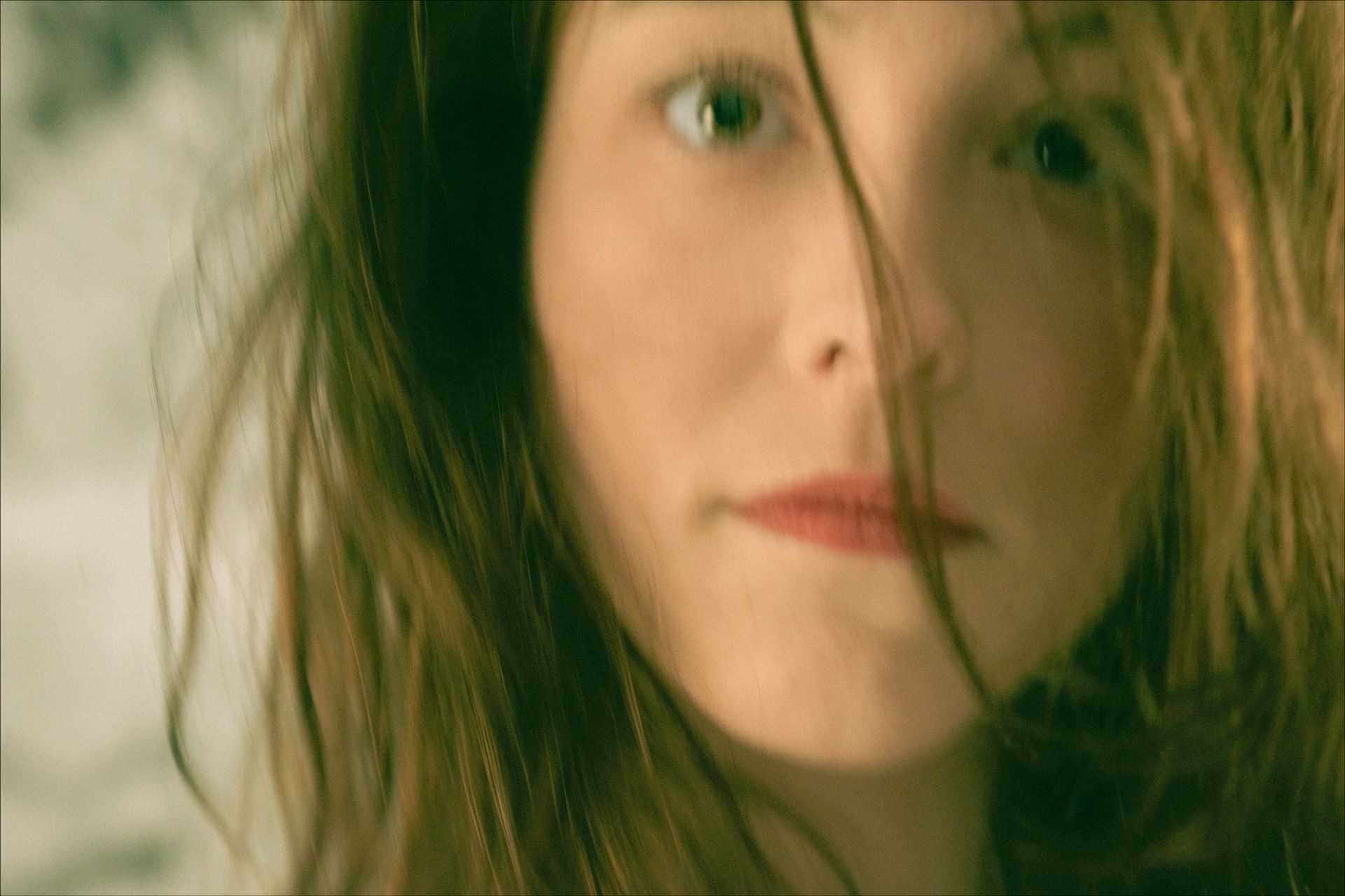 Woman with brown hair, part of it covering her face, looking at the camera.