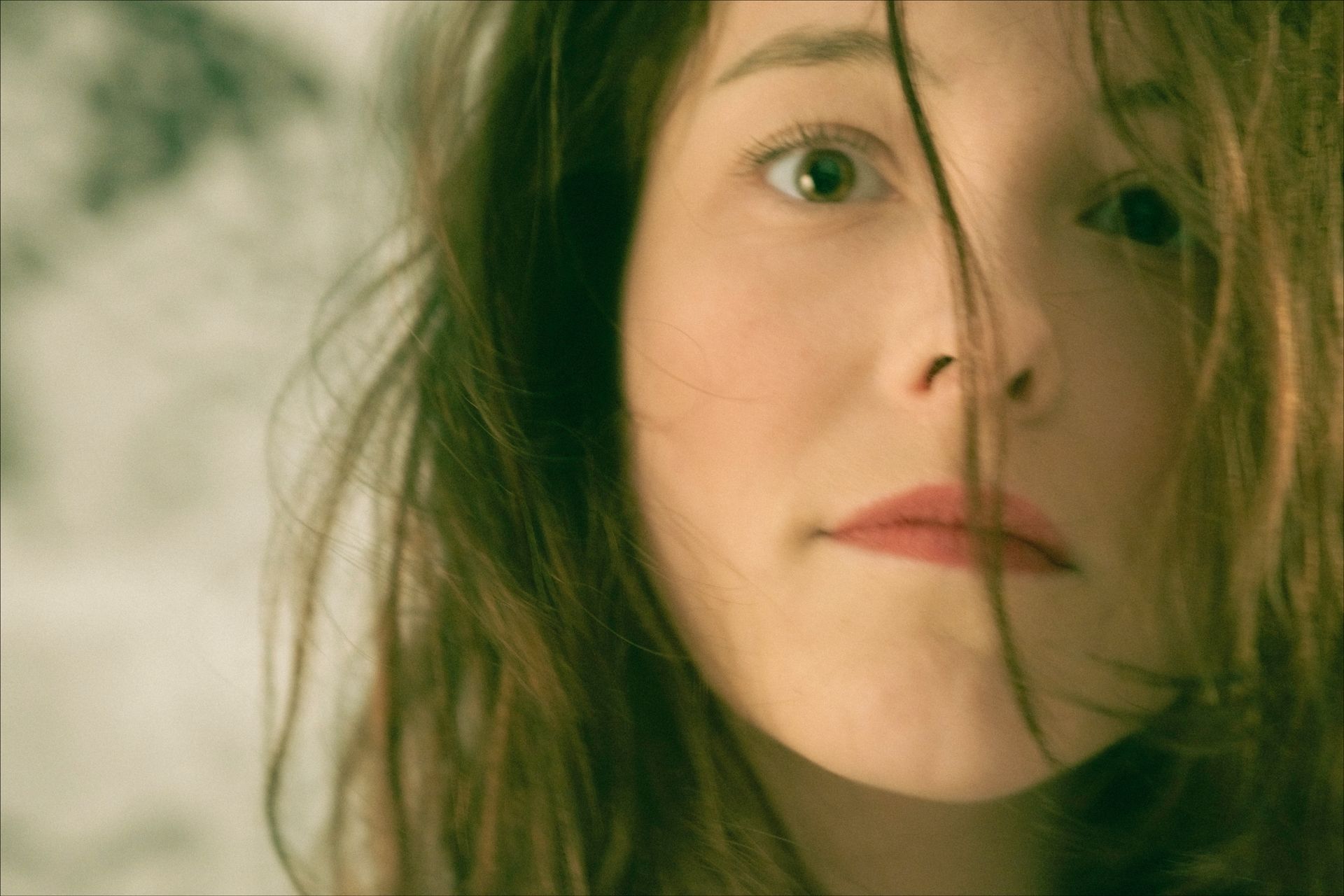 Woman with messy brown hair, looking at the camera. A strand of hair across her face, pale skin.