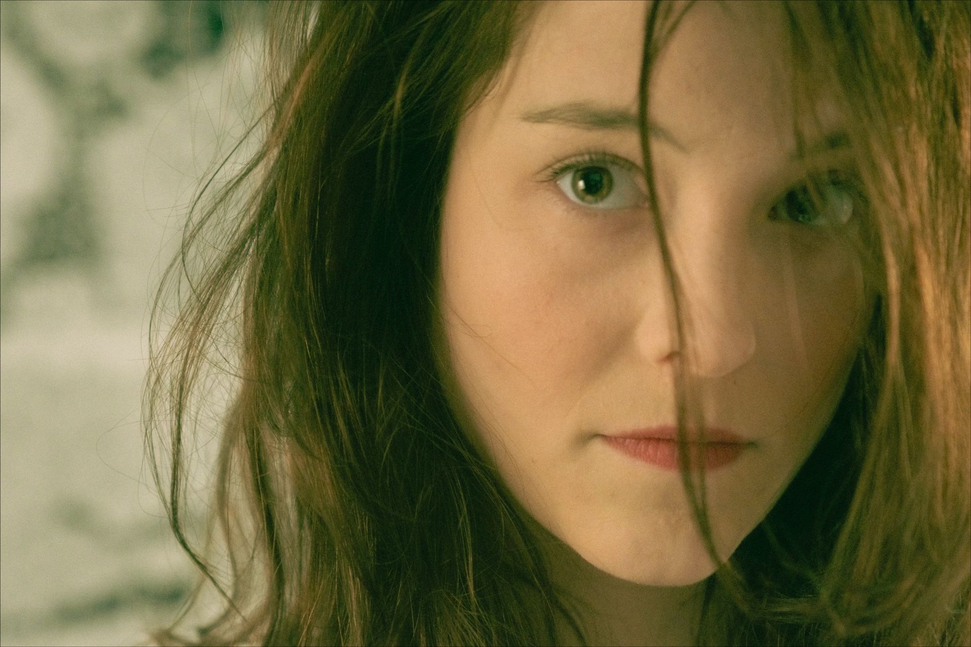 Woman with light skin stares directly at the viewer with an intense expression; hair falls over her face.