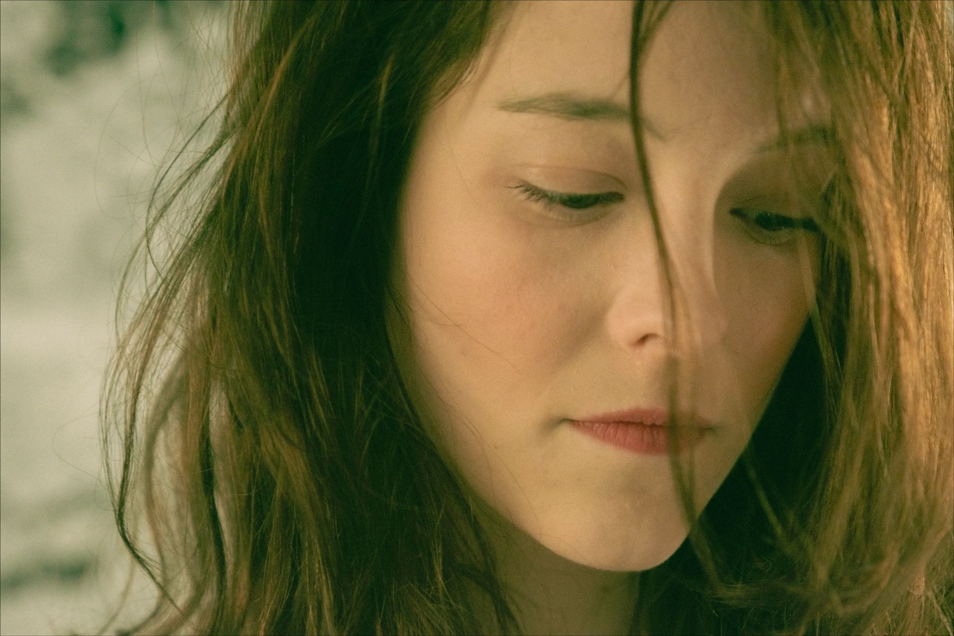 Woman with brown hair, looking down, softly lit.