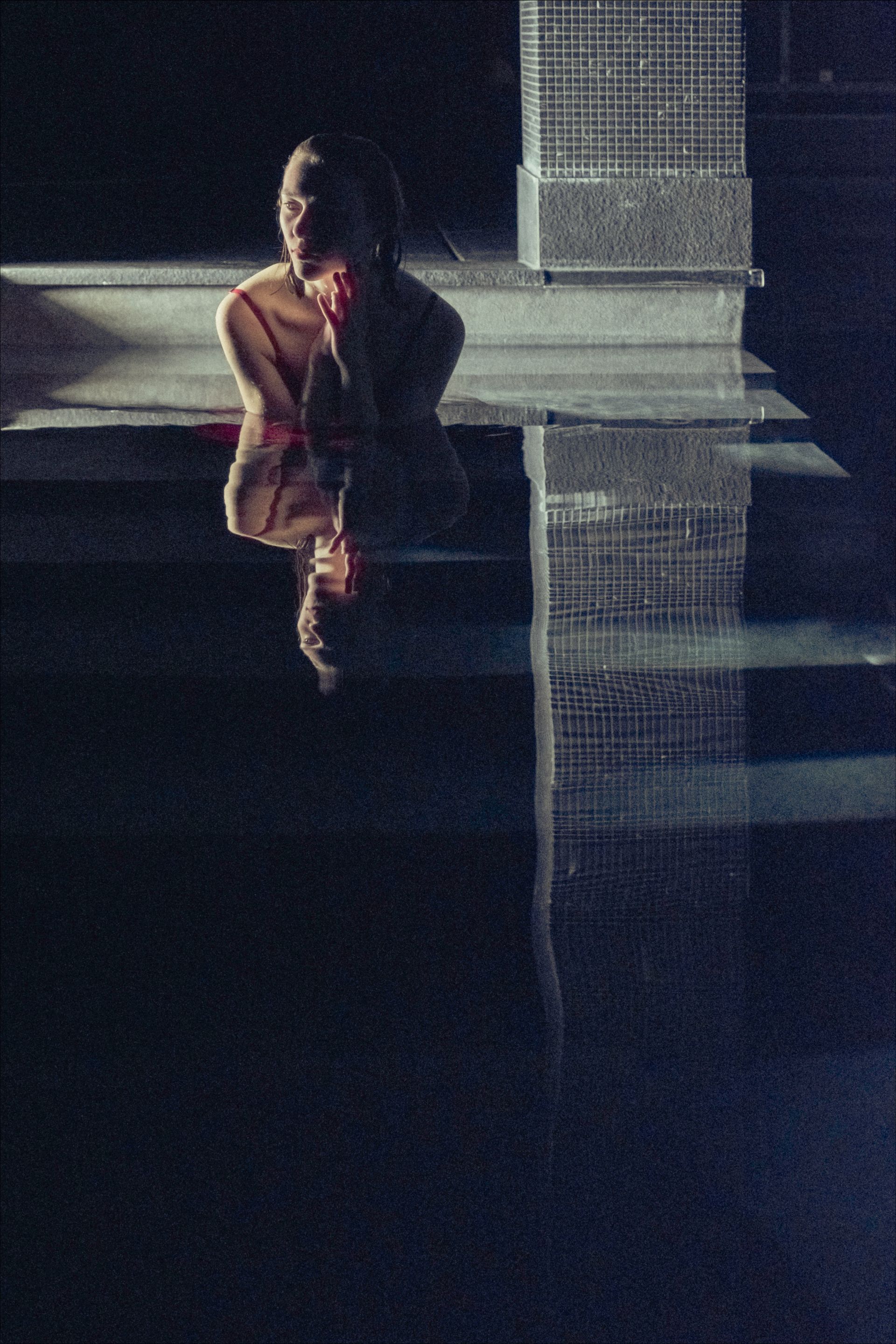 A person in a pool, reflected in water. Dark, moody scene.