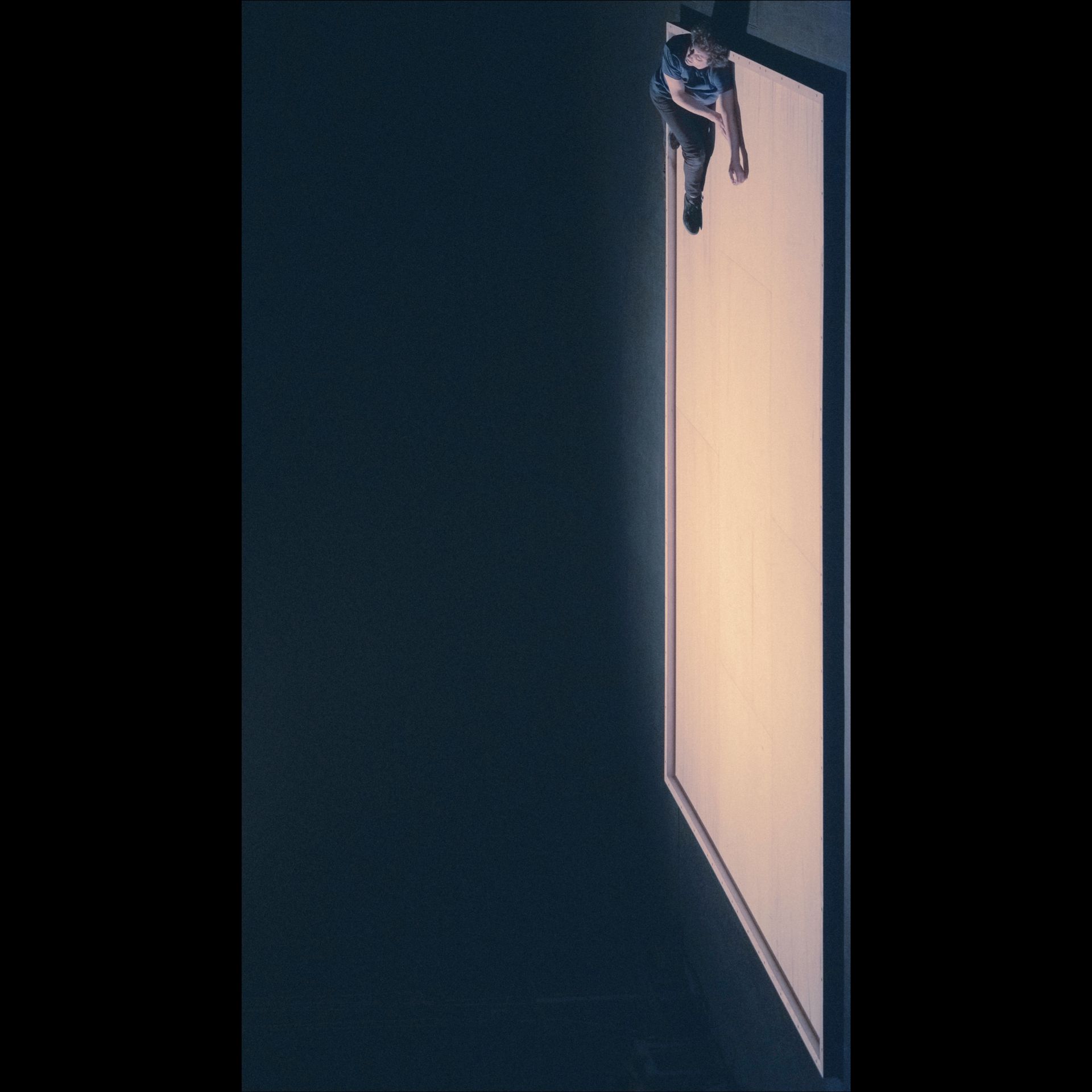 Person walking on a large, illuminated panel, with dark background.