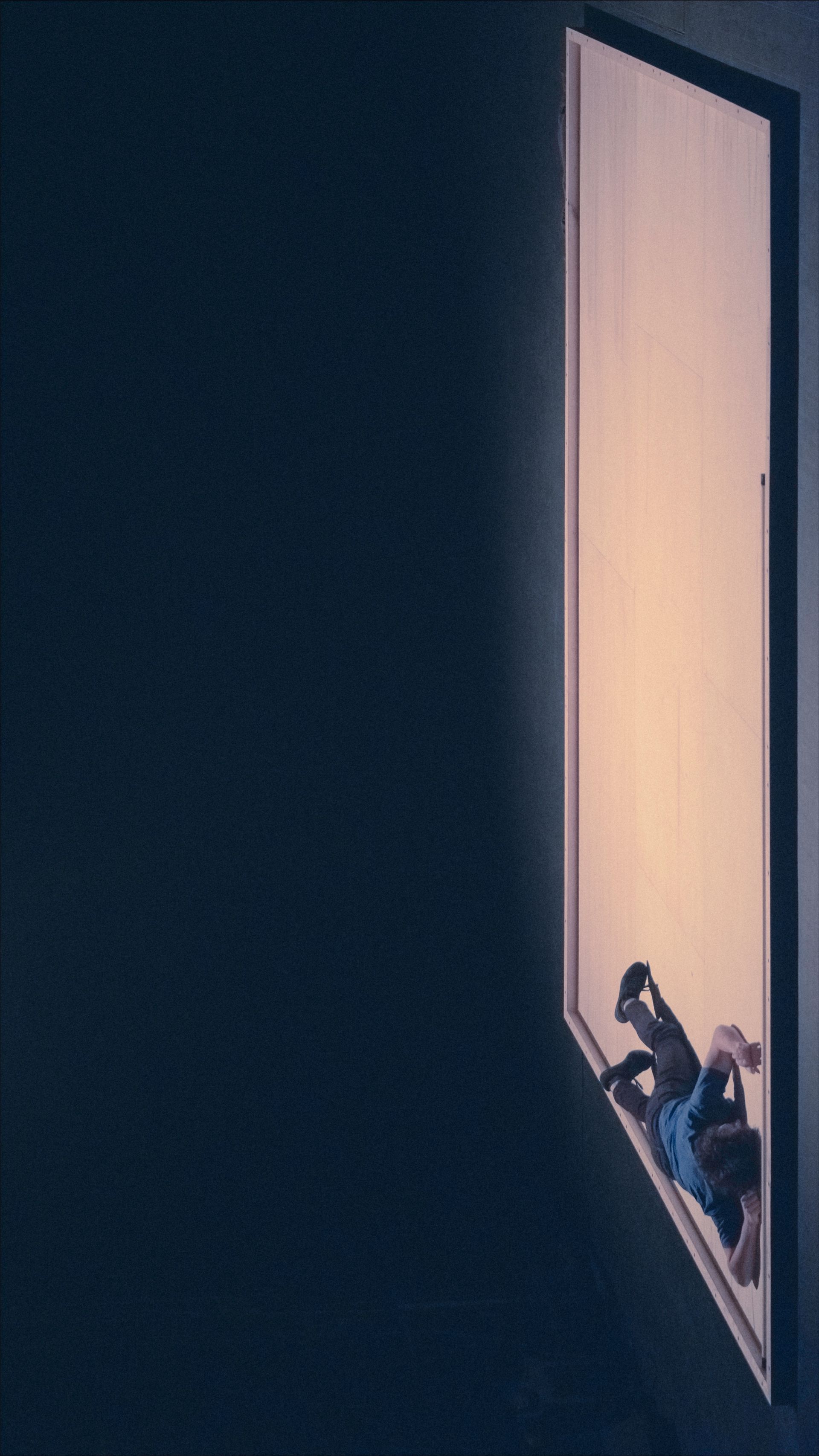 Person scaling a bright, angled doorway; dark background.