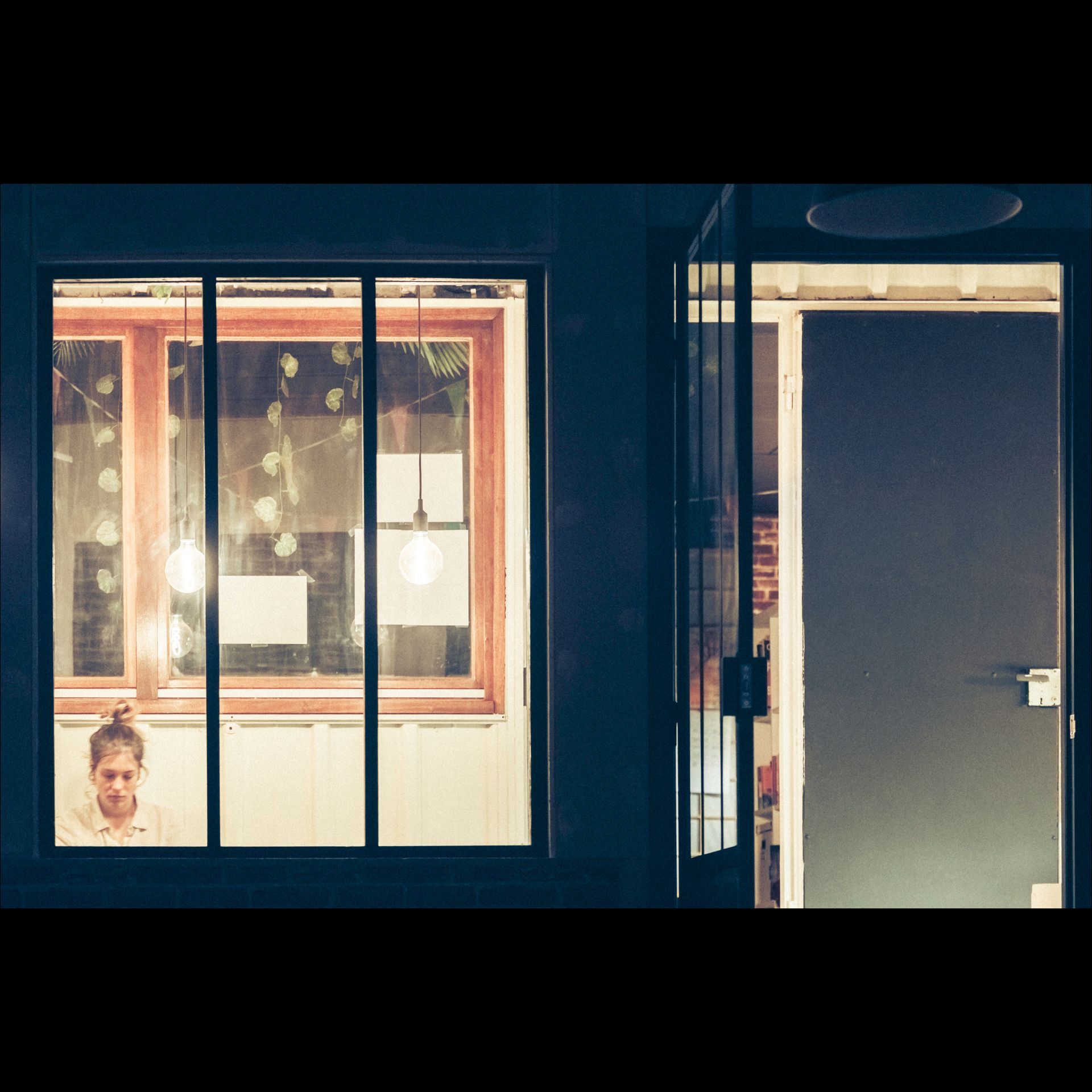 A person at a window, lit by indoor lights. Next to it, an open door, with light from the inside.