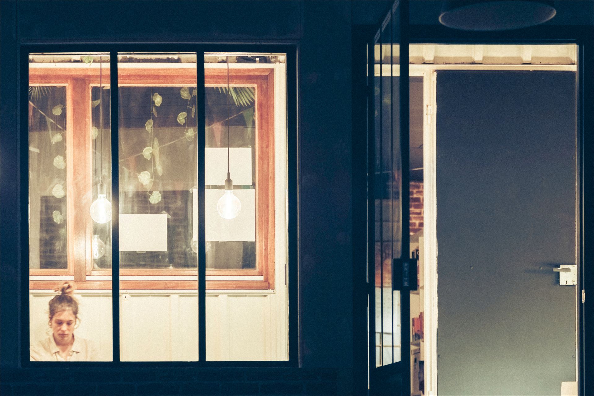 Person working in a window, lit from within, next to an open door.