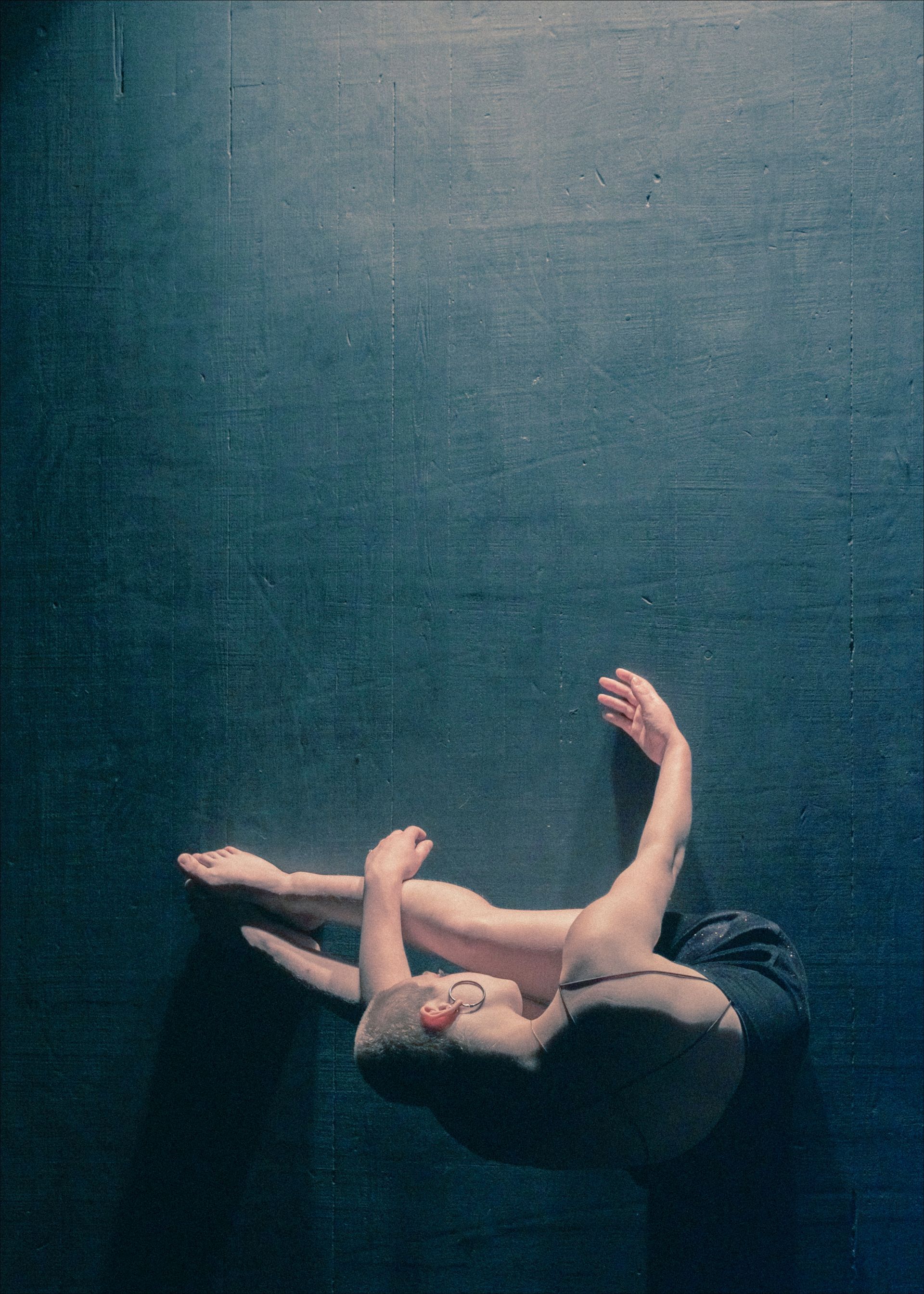 Dancer lies on dark blue floor, arms and legs extended in a graceful pose.