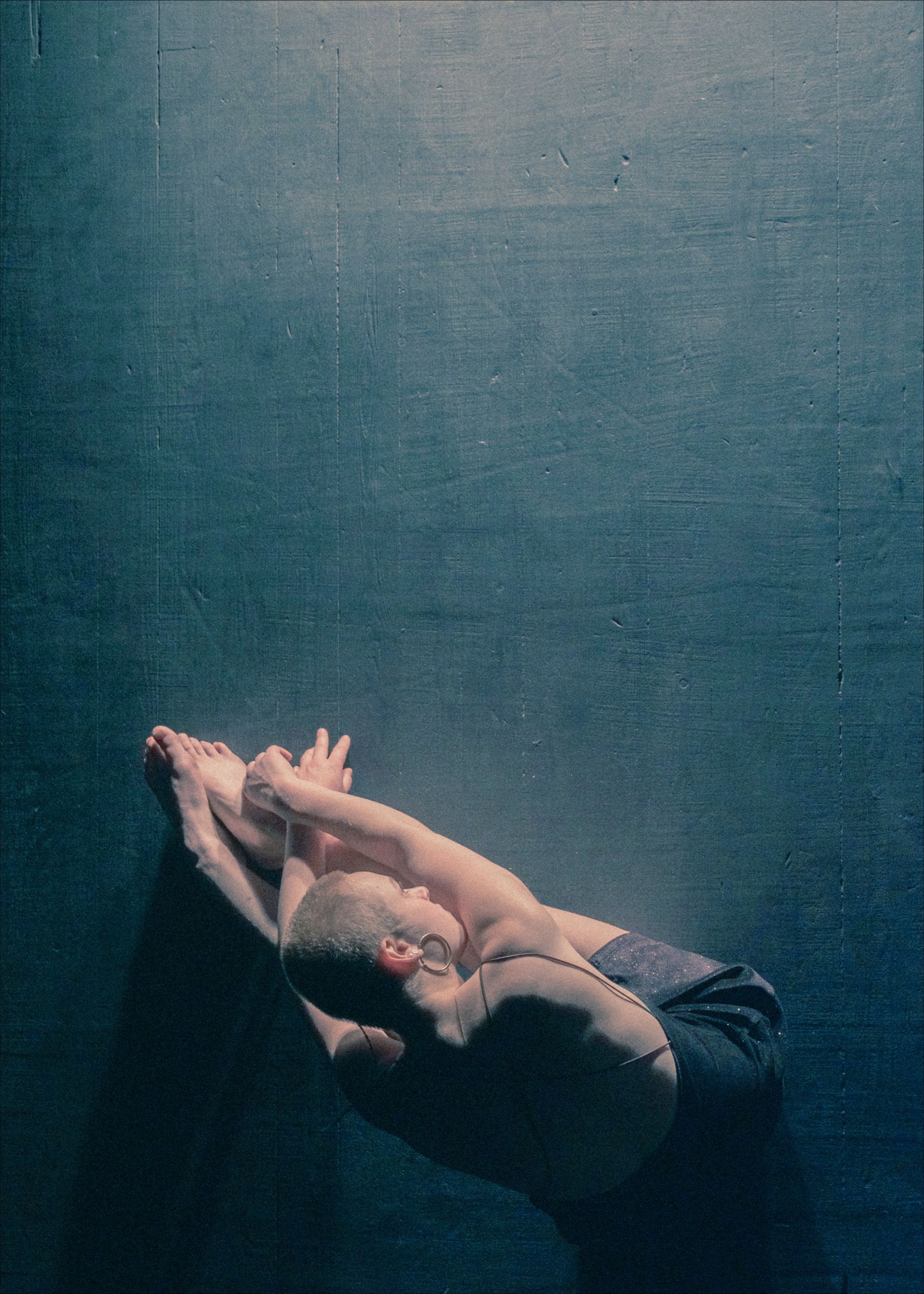 A person curled on a dark floor, knees to chest, arms wrapping around body.