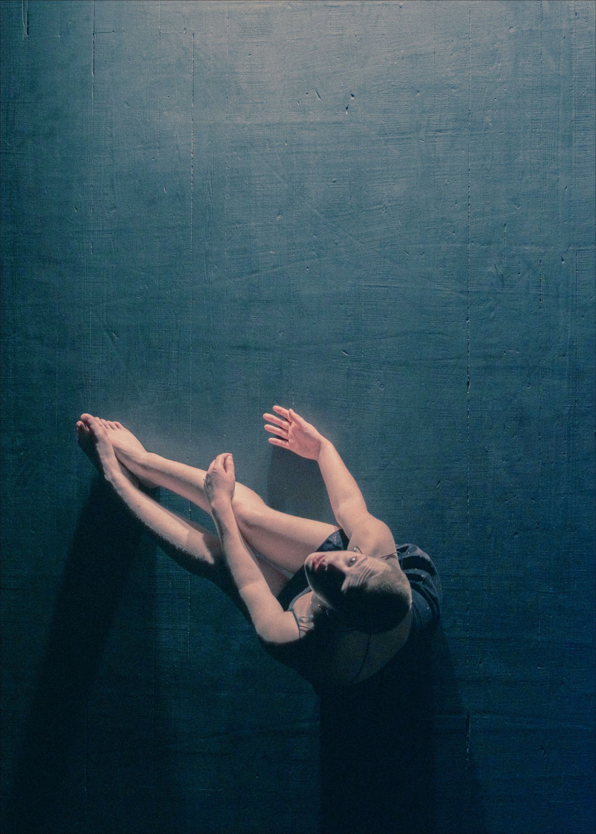 A dancer stretches on a dark blue floor, arms and legs extended.