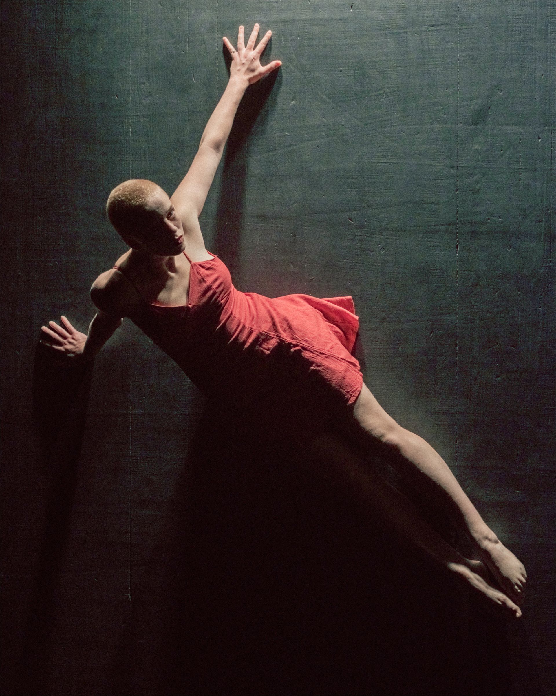 Dancer in a red dress, arms outstretched, on a dark surface, possibly performing.