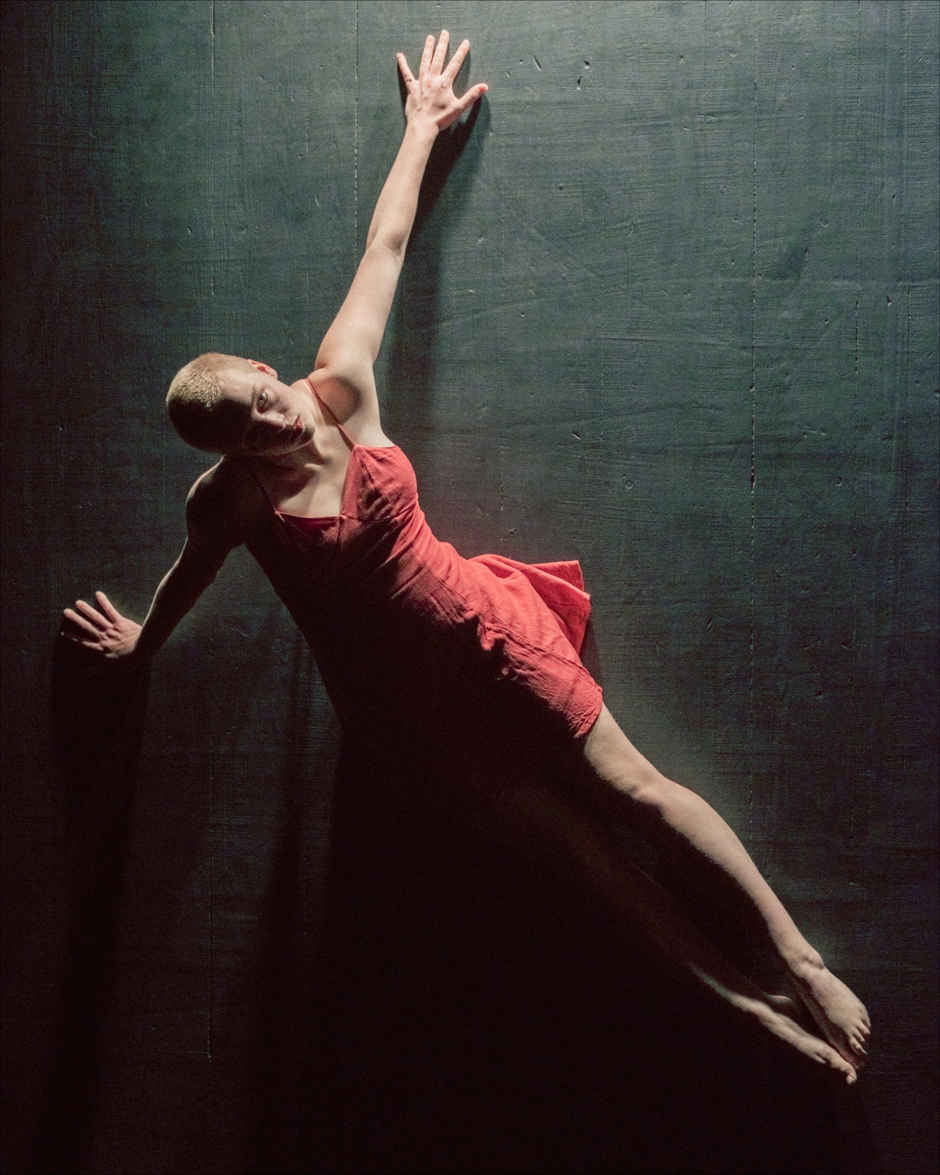 A dancer in a red dress floats on a dark surface, one arm reaching up.