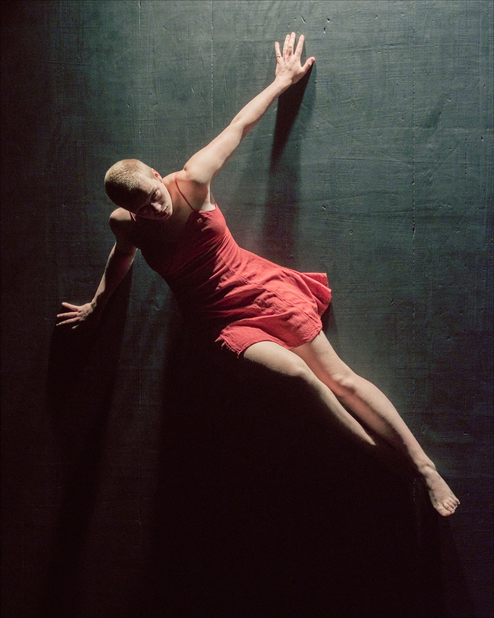 Dancer in a red dress lies on a dark surface, arms extended, lit from above.