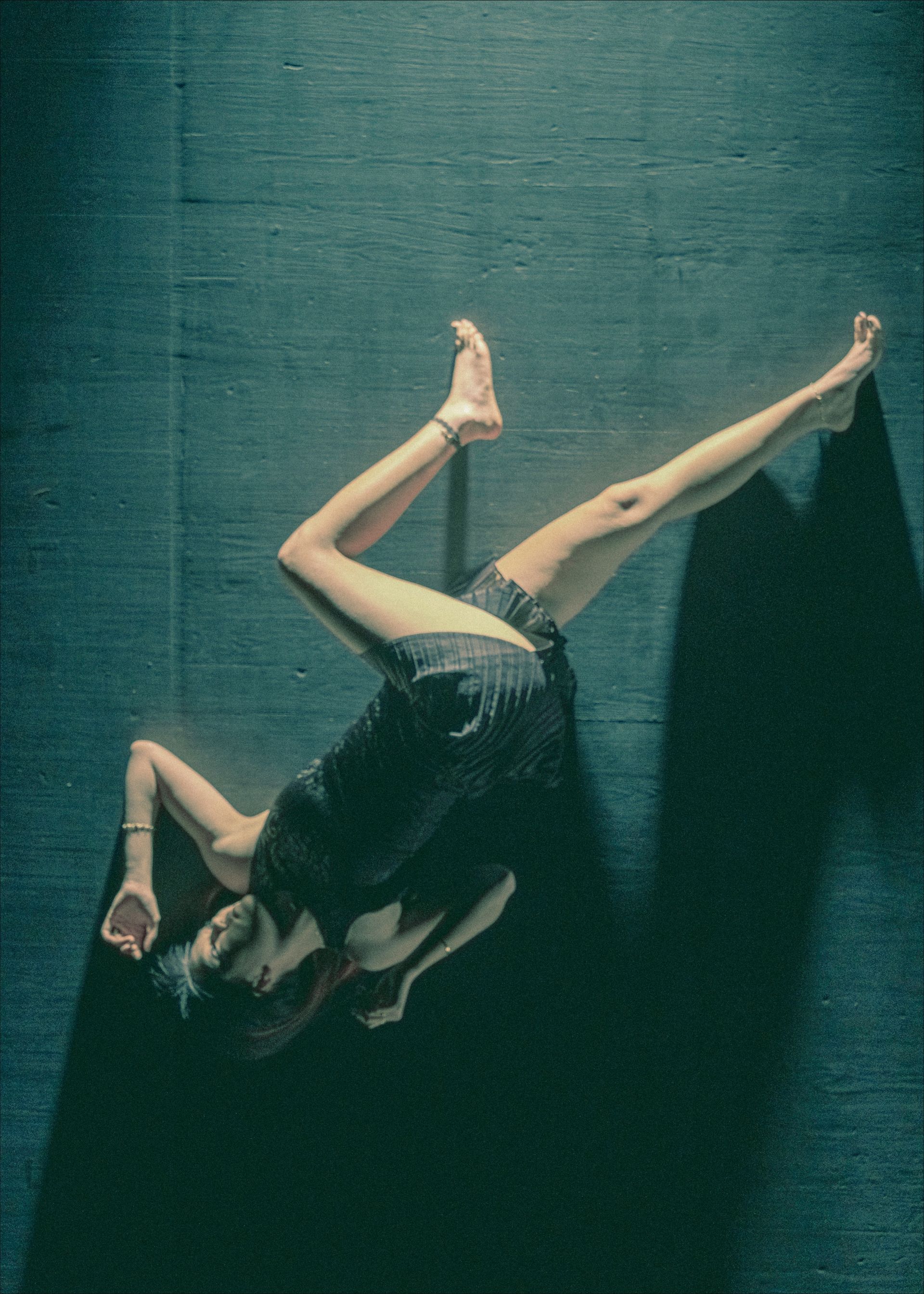 Dancer in a dark room, lying diagonally with one leg raised. Dark dress, arm raised. Shadow.