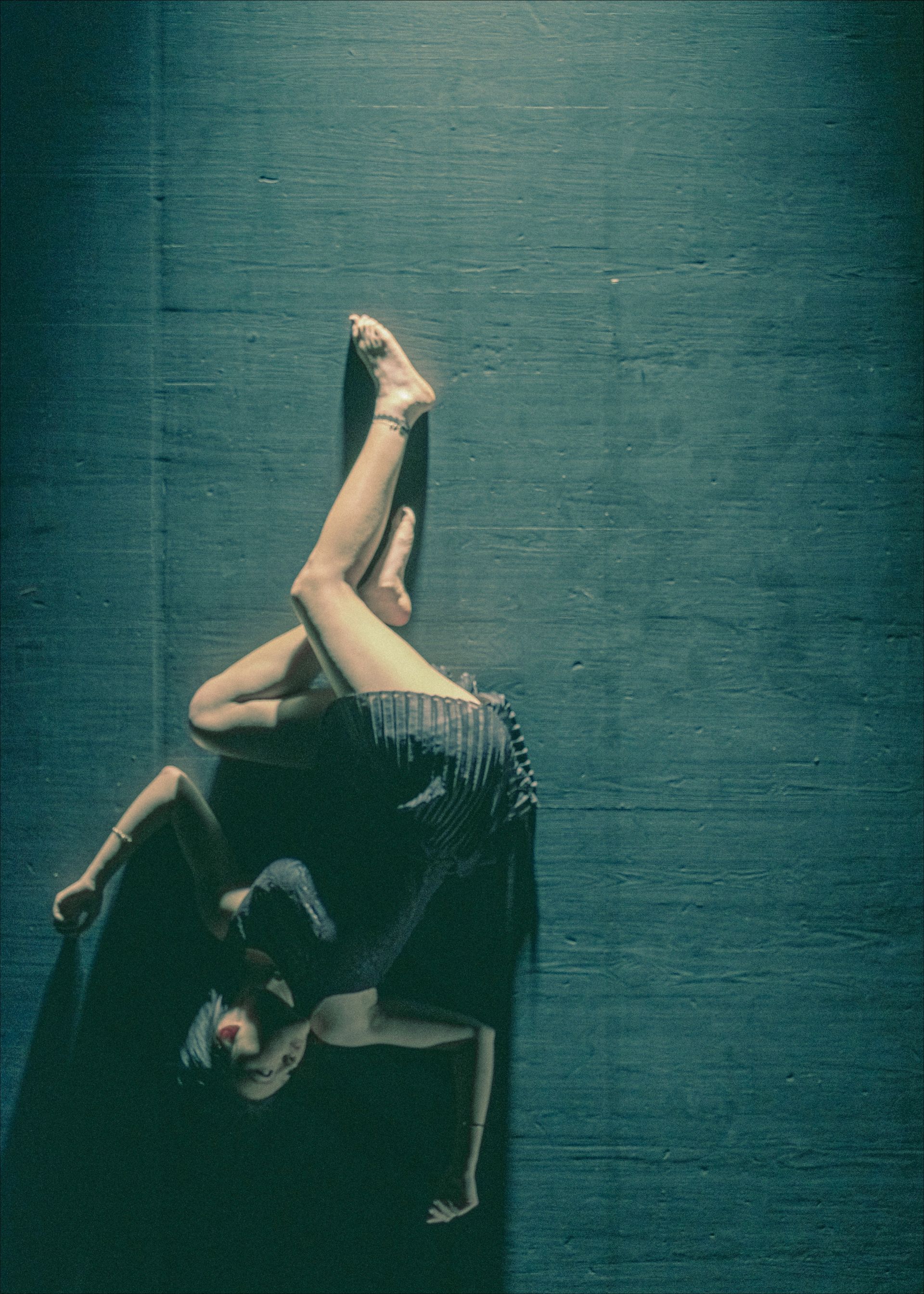 A person in a dark dress is in a yoga pose on a blue textured floor, lit by a spotlight.